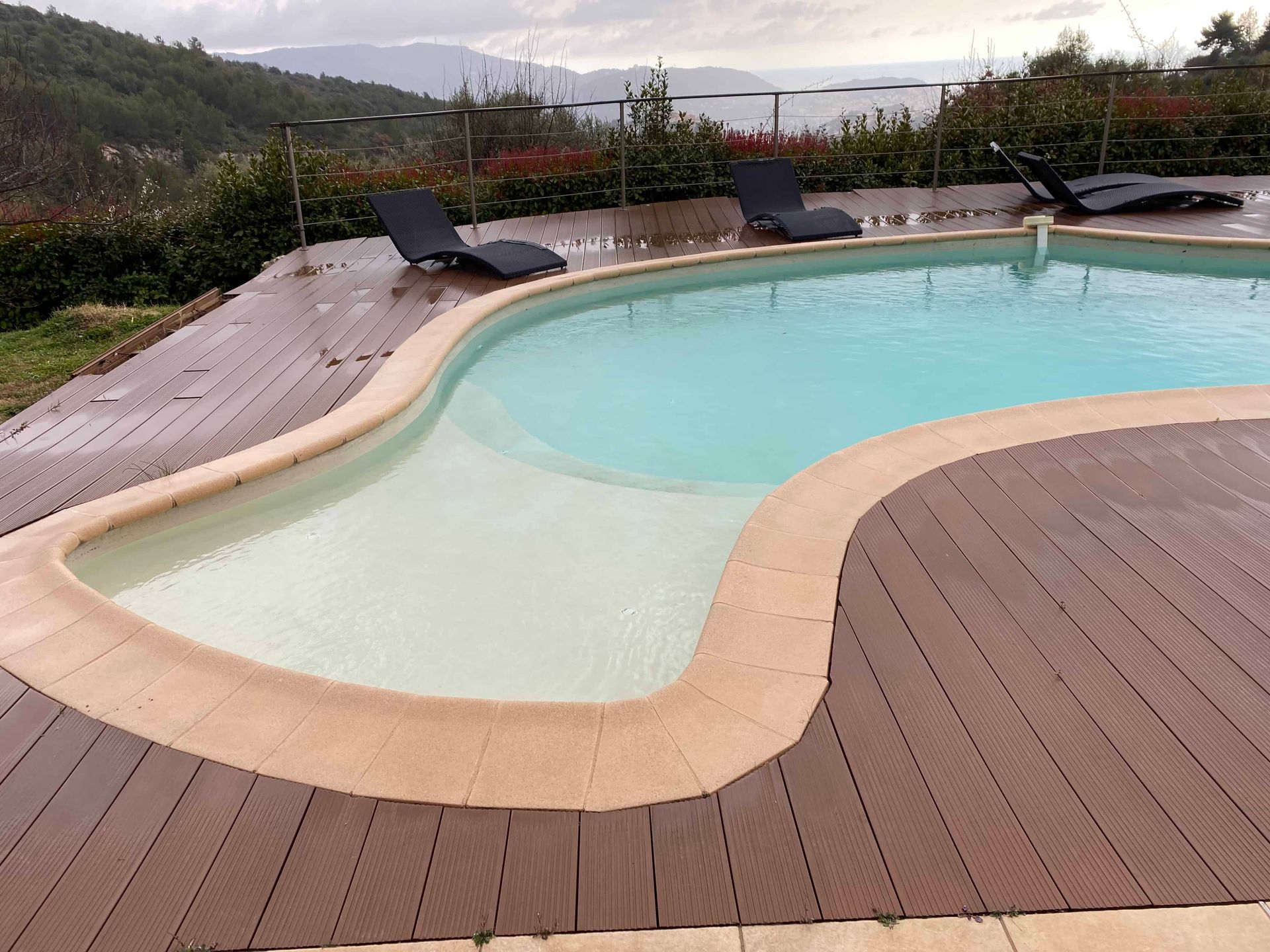 Une grande piscine avec une terrasse en bois et des chaises autour