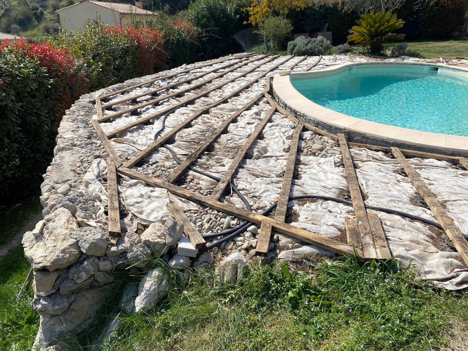 Une piscine est entourée d'un mur de pierre et d'une terrasse en bois.