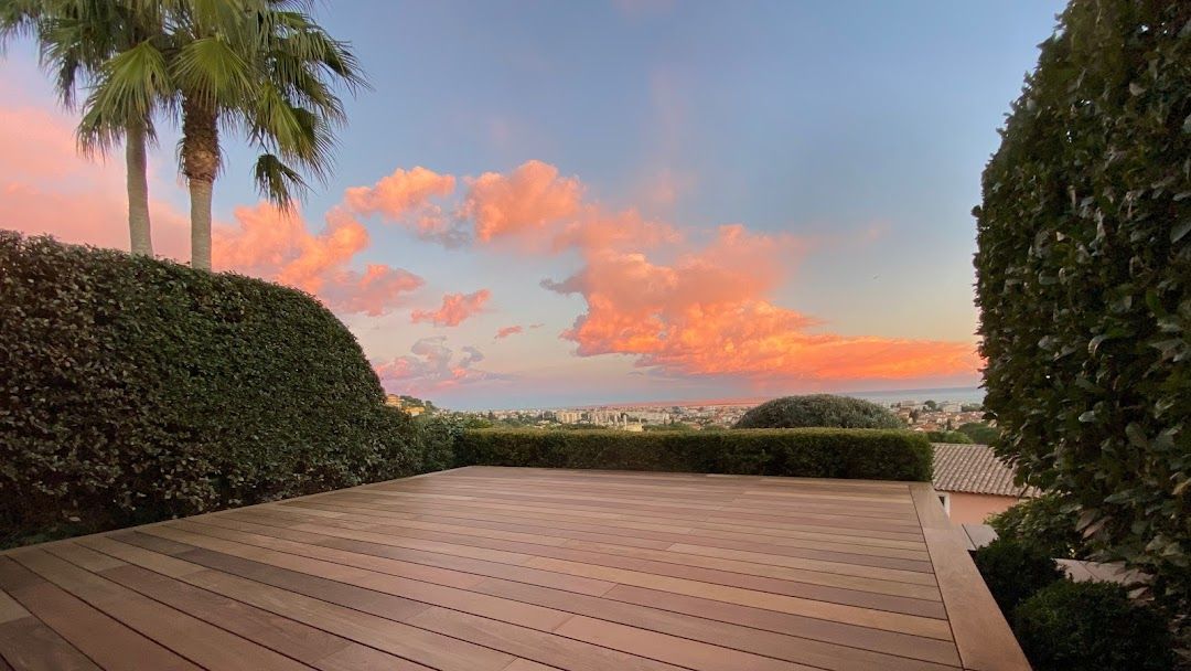 Il y a un coucher de soleil en arrière-plan et une terrasse en bois au premier plan.