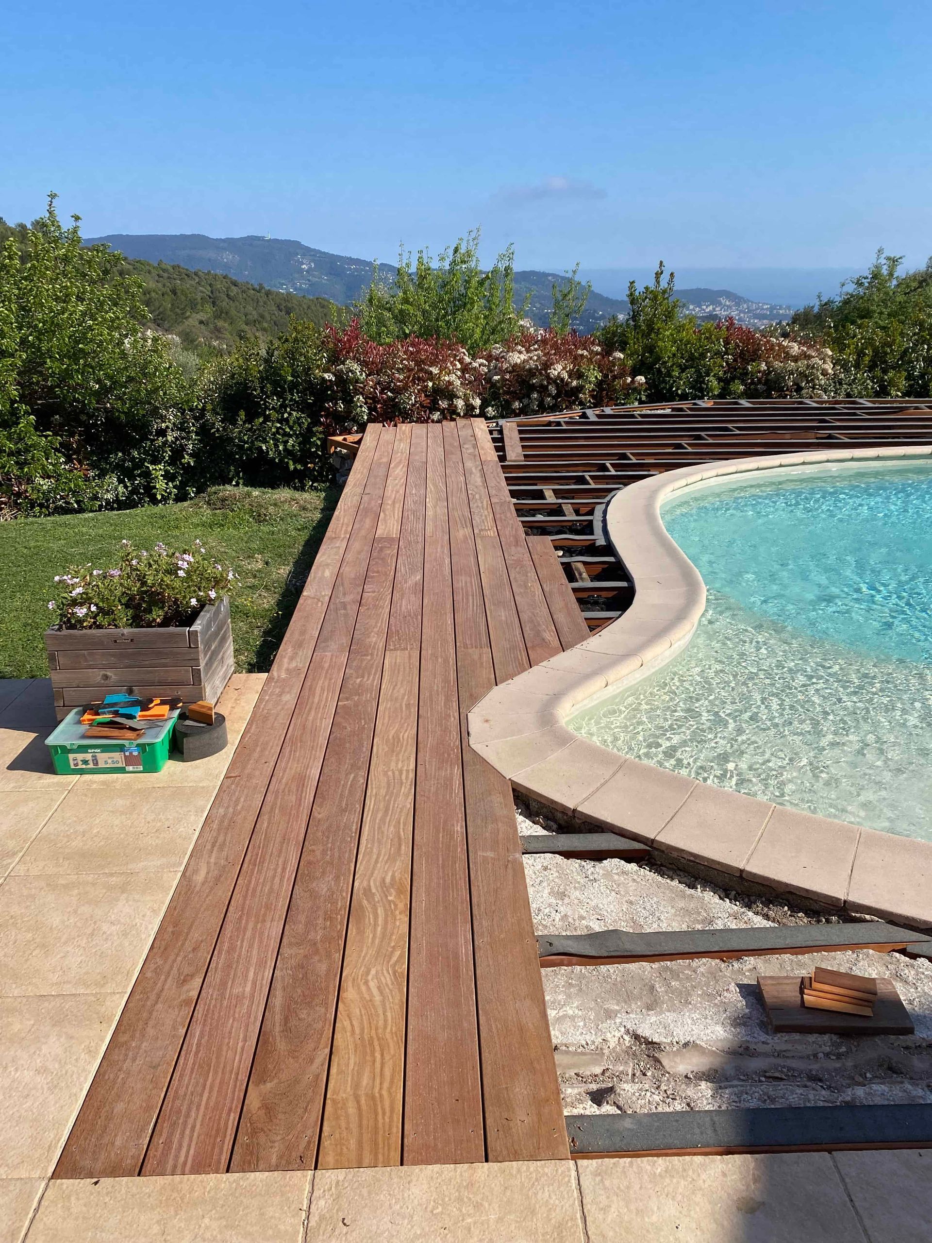 Une terrasse en bois est en cours de construction à côté d'une piscine.