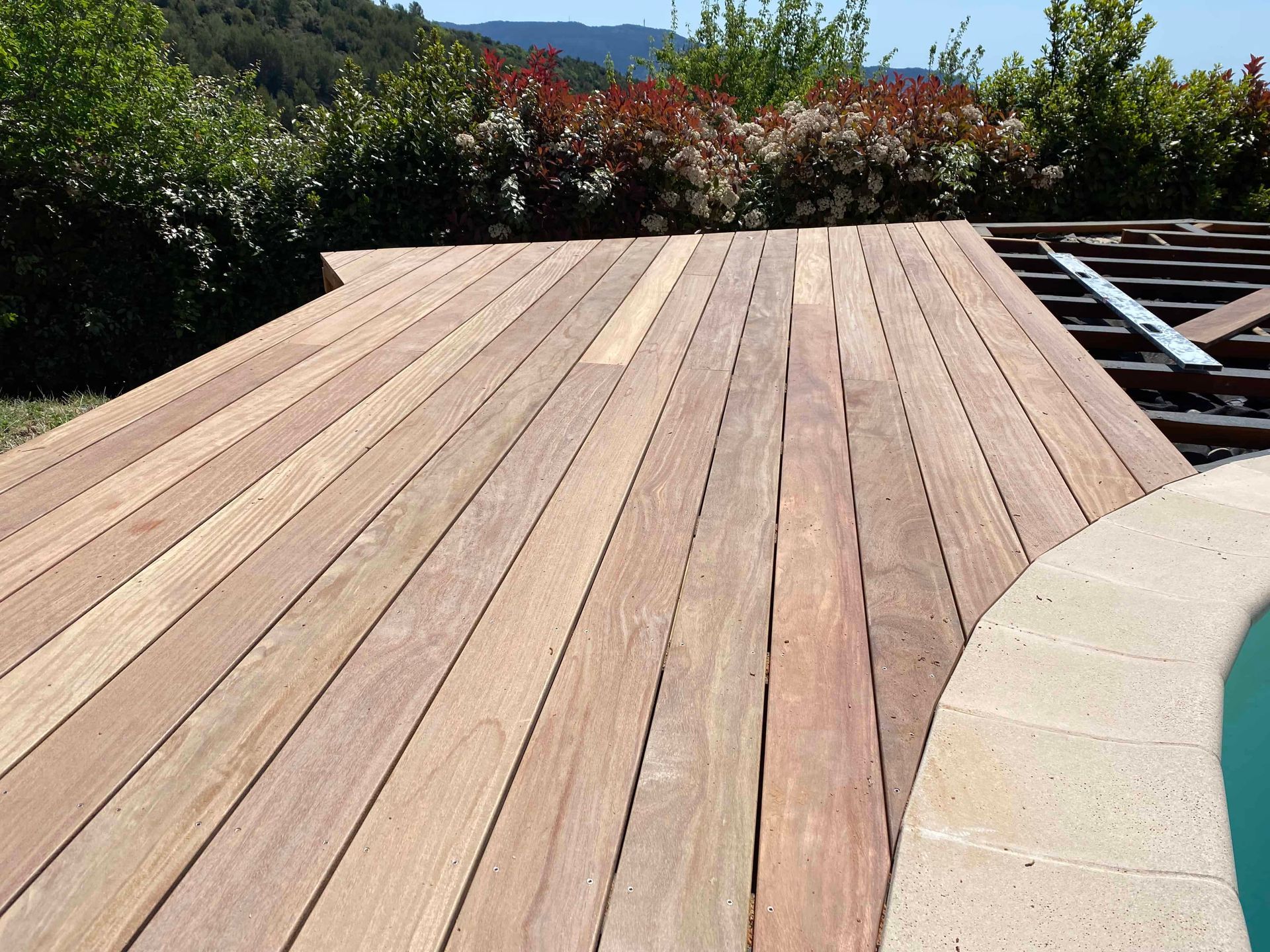 Une terrasse en bois avec une piscine en arrière-plan