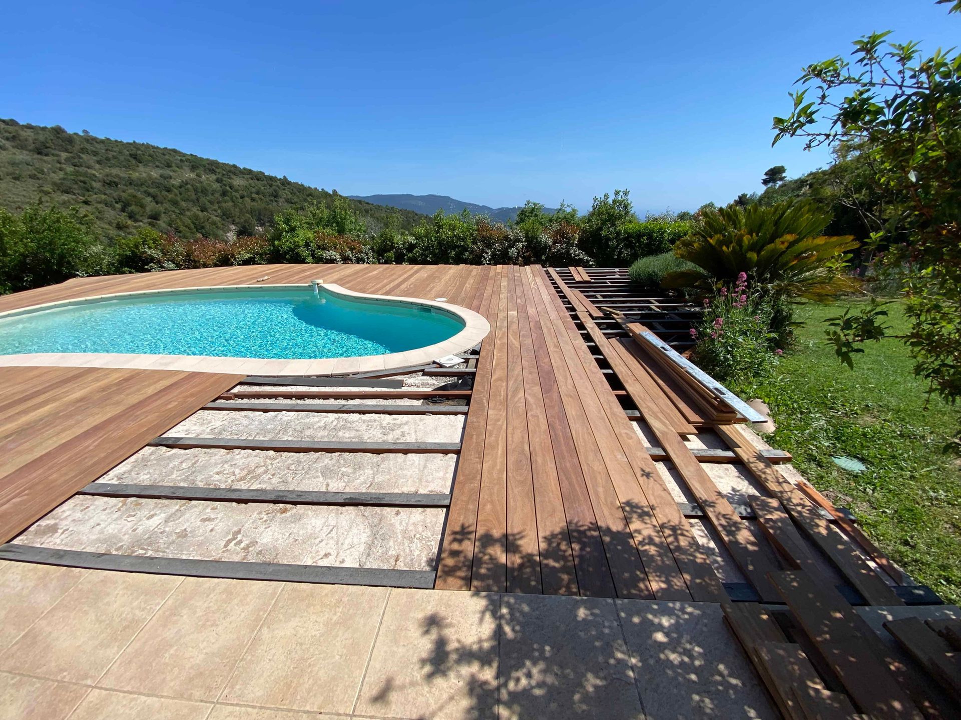 Une terrasse en bois avec une piscine en arrière-plan