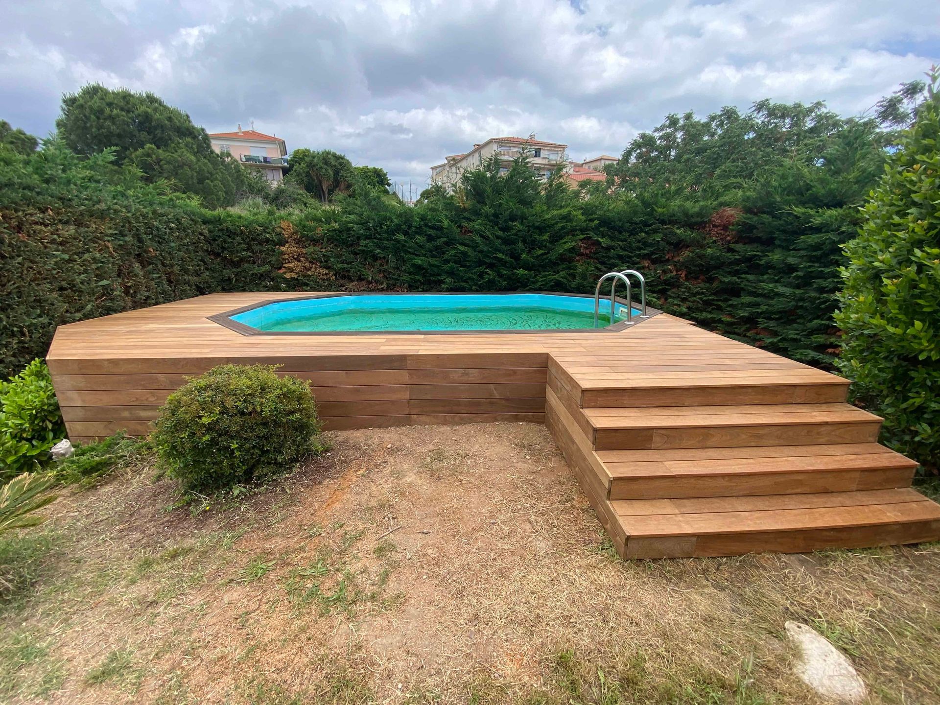 Une petite piscine entourée d'arbres et d'une terrasse en bois.