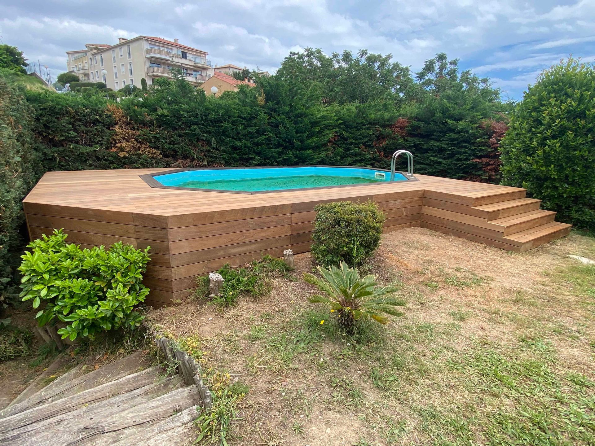 Une grande piscine est entourée d'une terrasse en bois et d'escaliers dans une cour arrière.