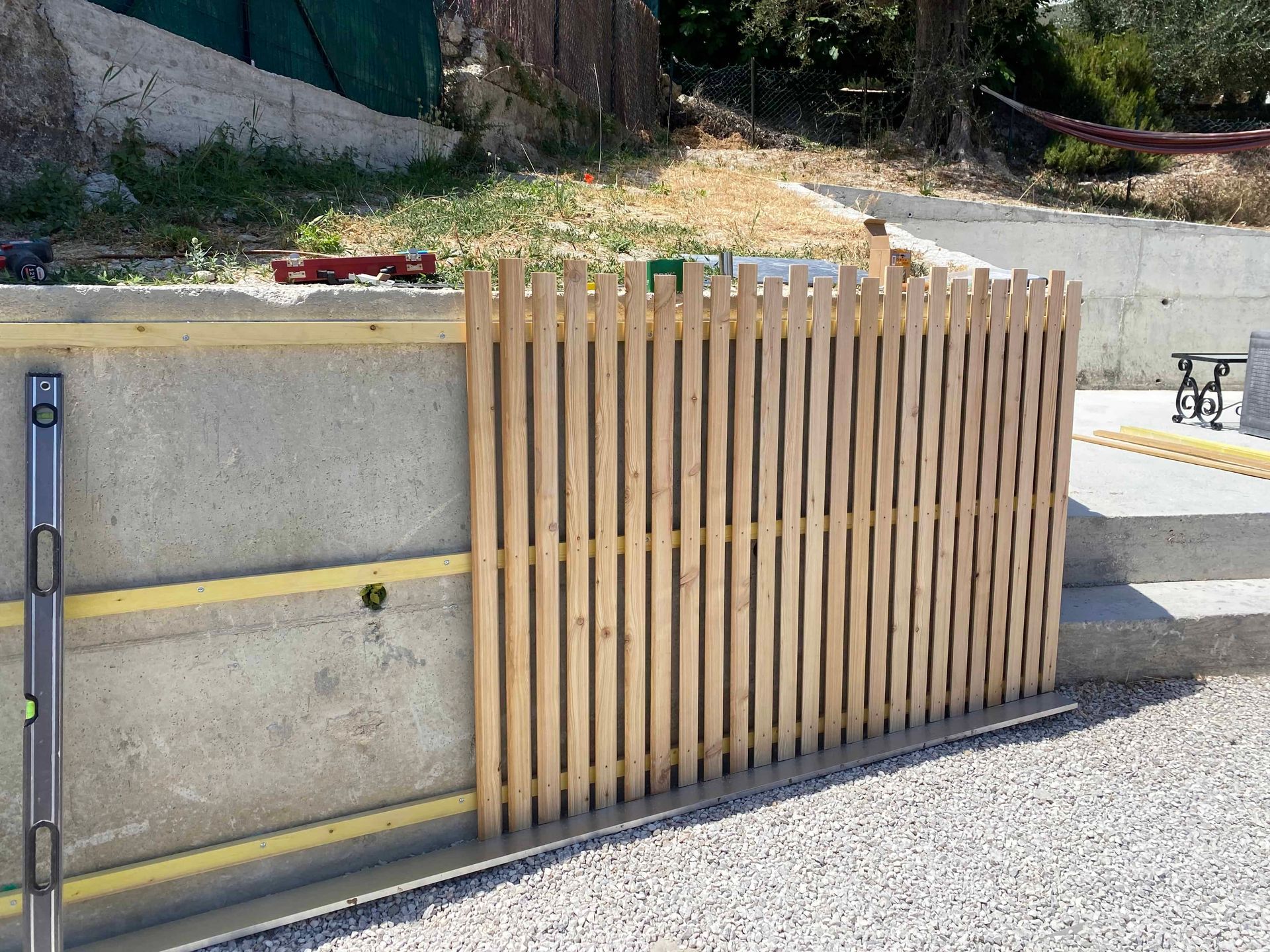 Une clôture en bois est en train d'être construite à côté d'un mur en béton.