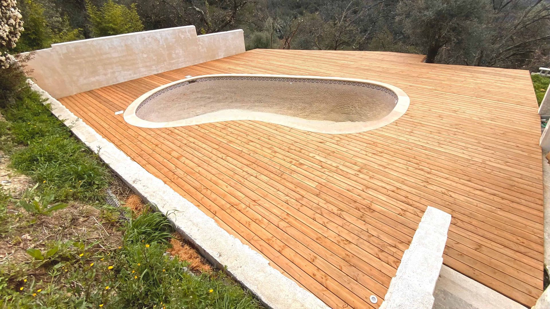 Une terrasse en bois avec une piscine en arrière-plan