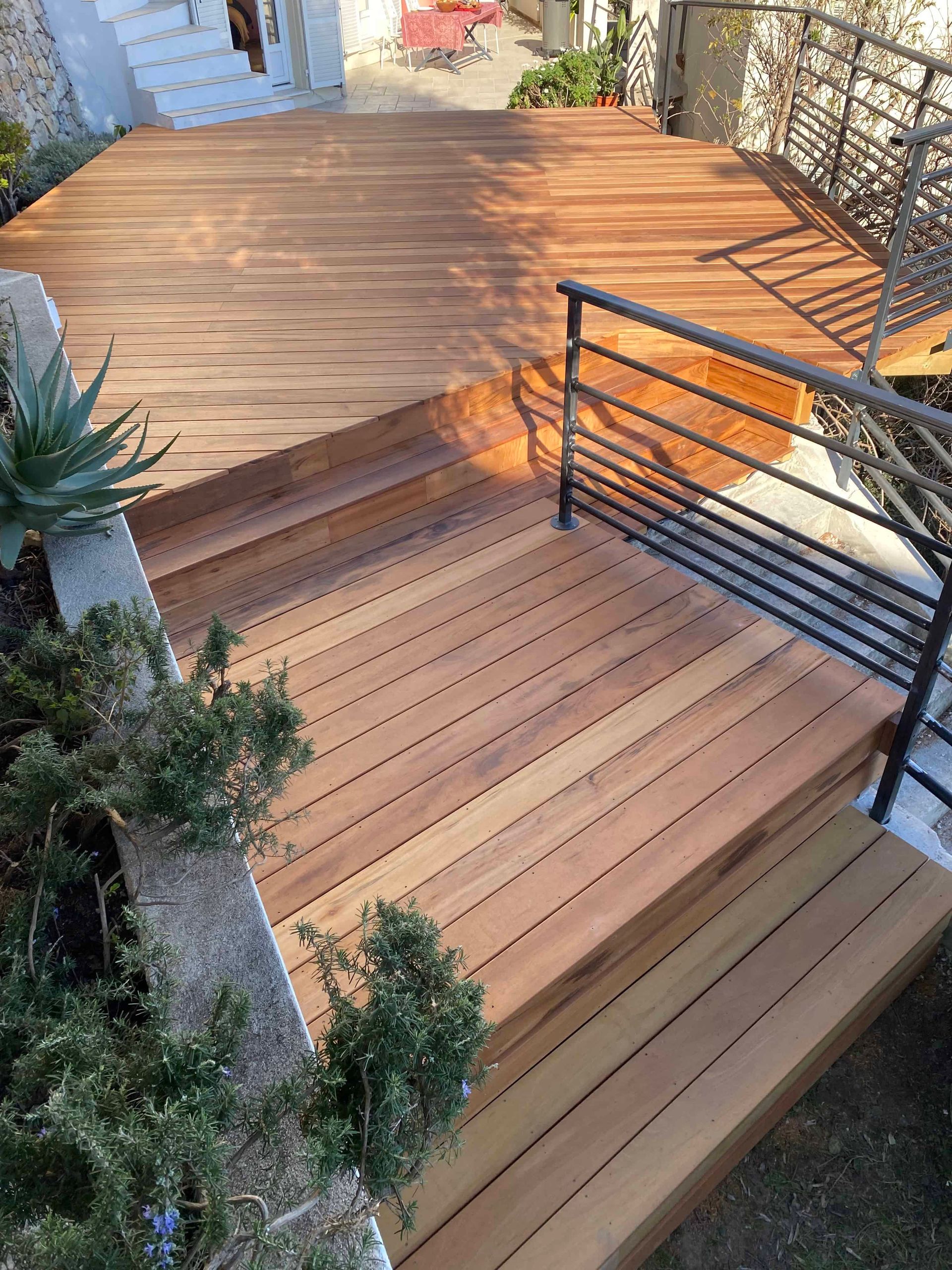 Une terrasse en bois avec des escaliers qui y mènent et une balustrade en métal.
