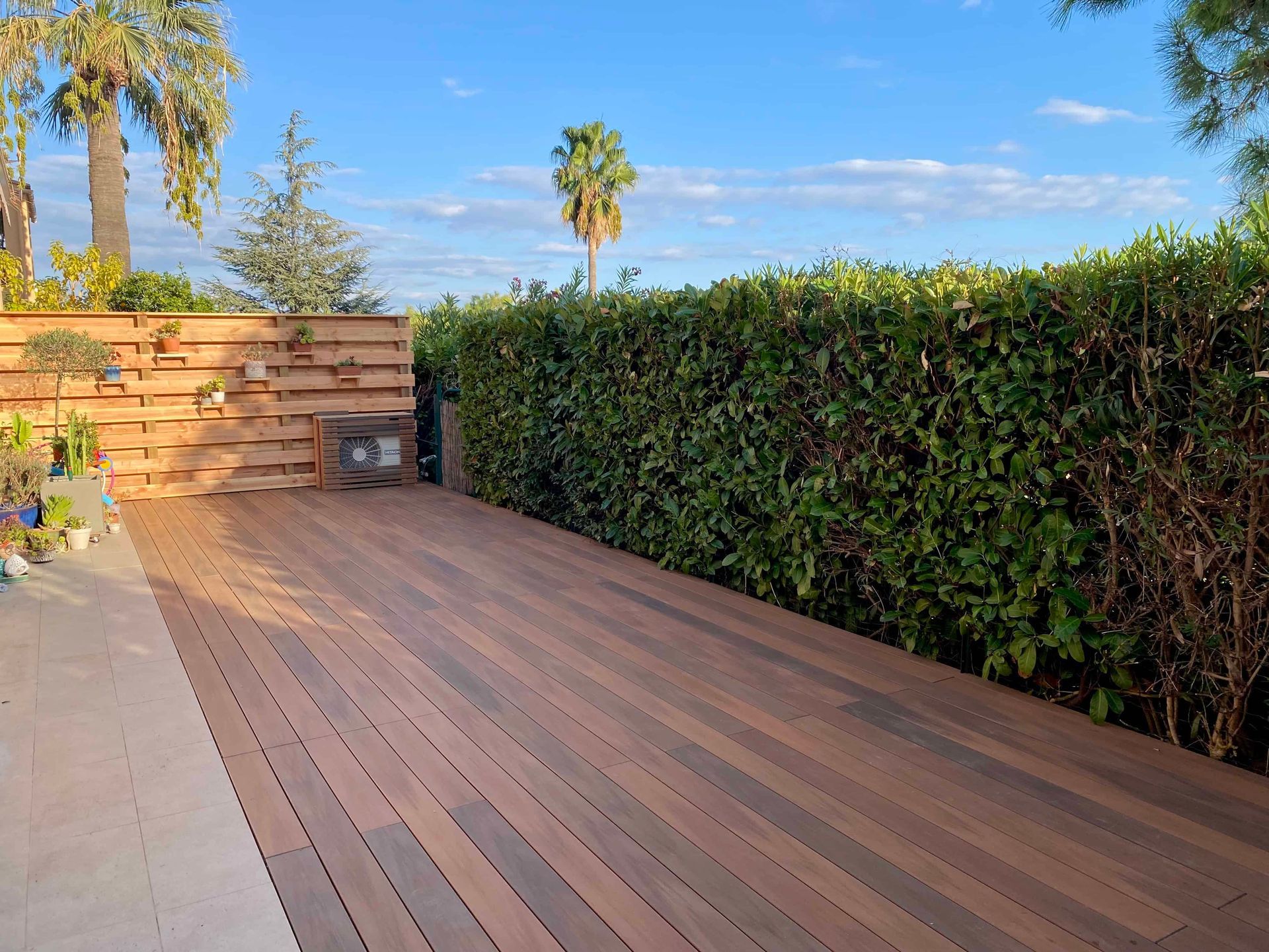 Une terrasse en bois est entourée d'une haie verte luxuriante.