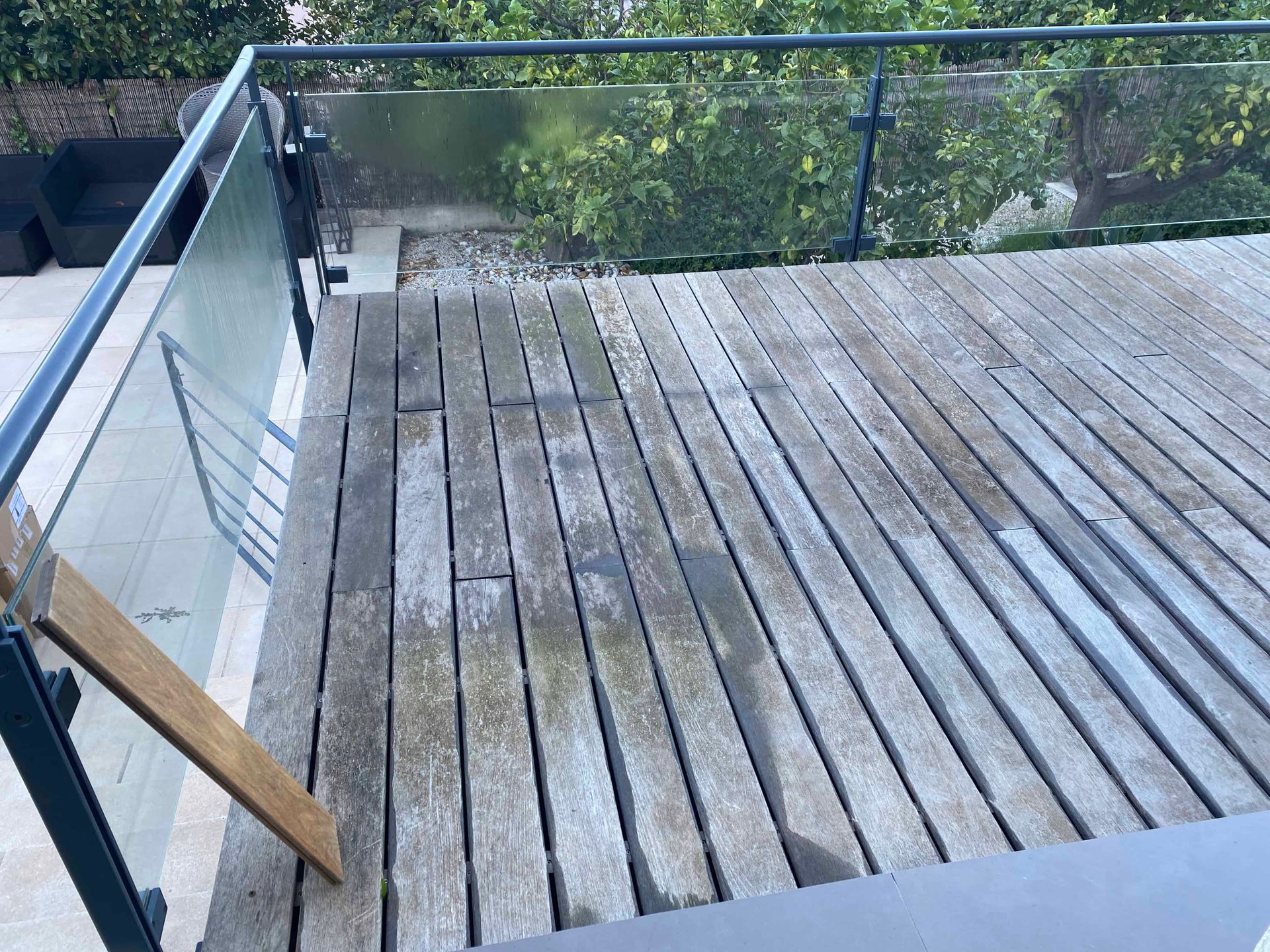 Une terrasse en bois avec une balustrade en verre et des escaliers qui y mènent.