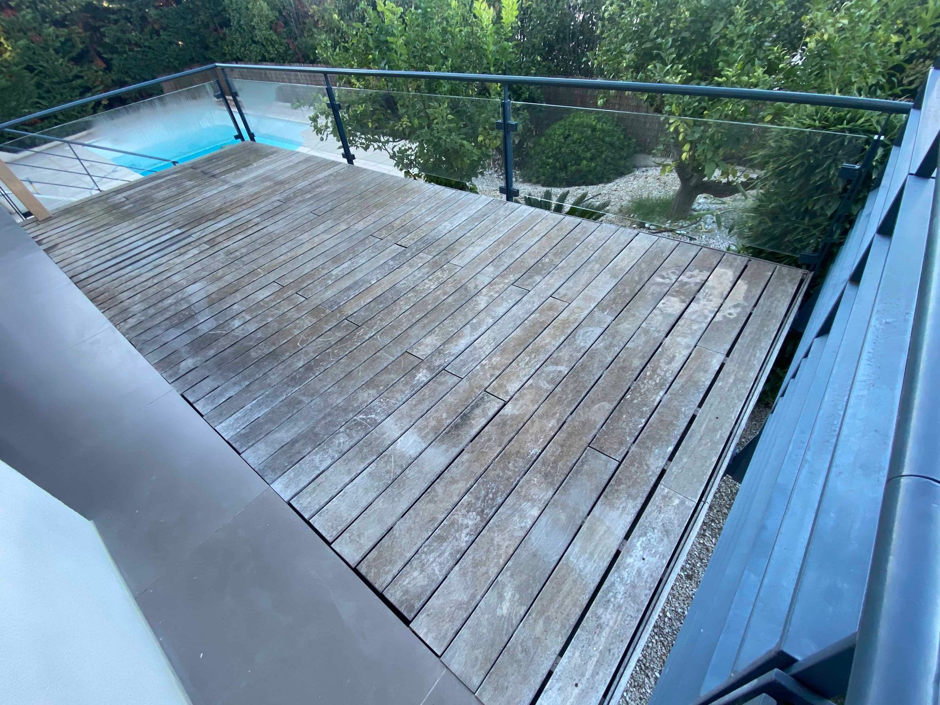 Une terrasse en bois avec une balustrade et une piscine en arrière-plan.