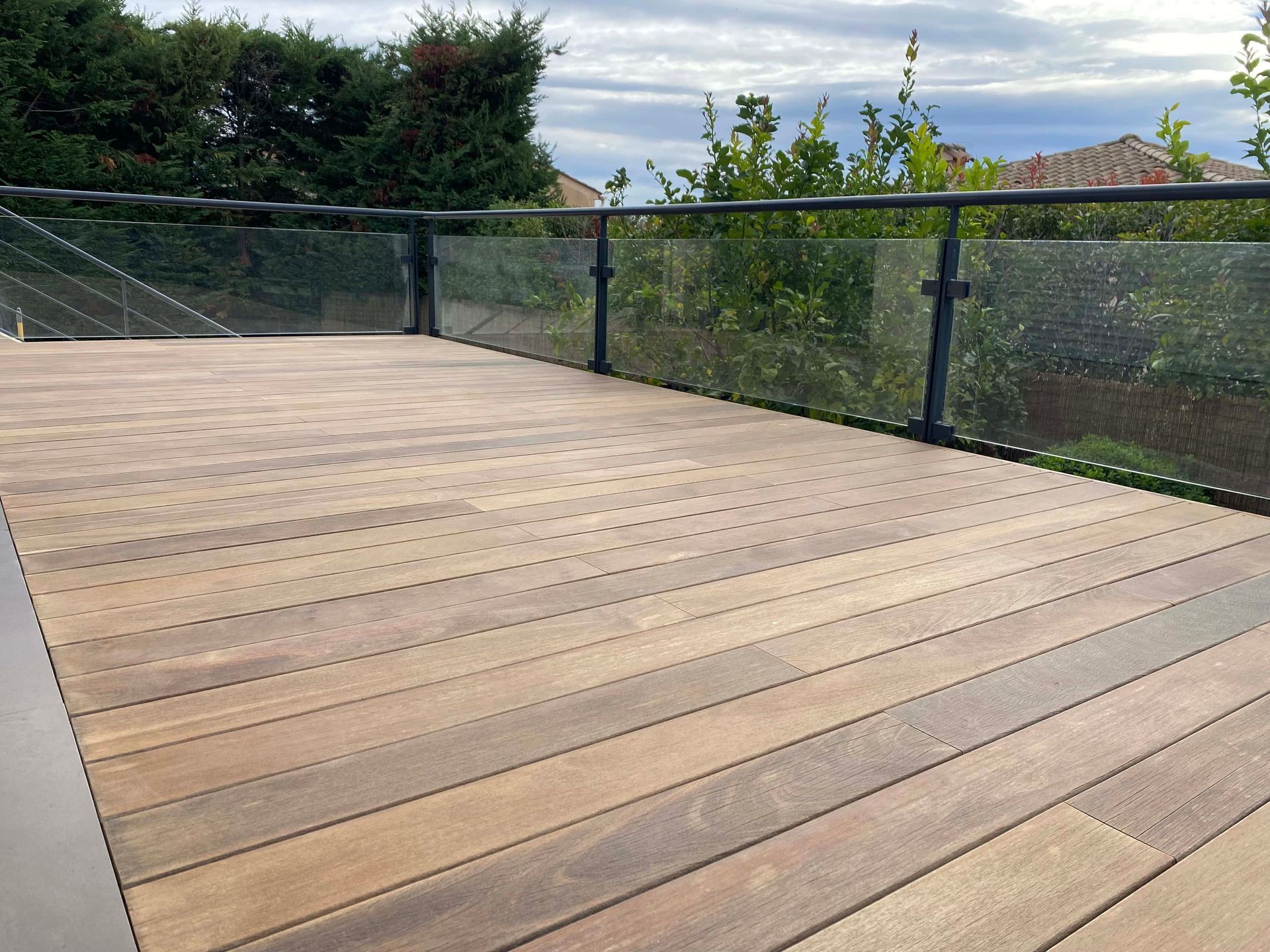 Une terrasse en bois avec une balustrade en verre et des arbres en arrière-plan.