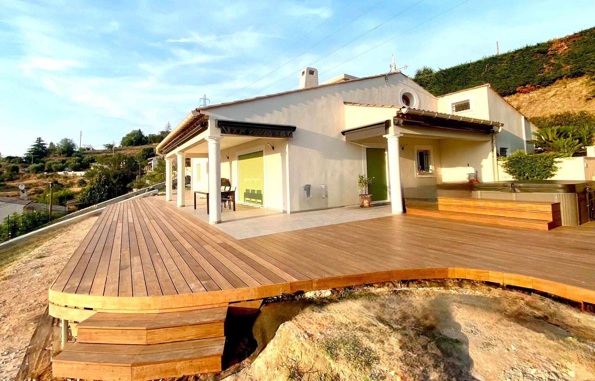 Une grande maison blanche avec une grande terrasse en bois devant elle.