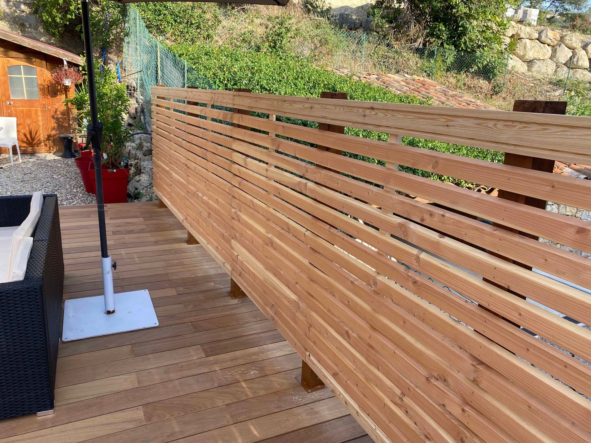 Une clôture en bois entoure une terrasse en bois avec une chaise et un parasol.