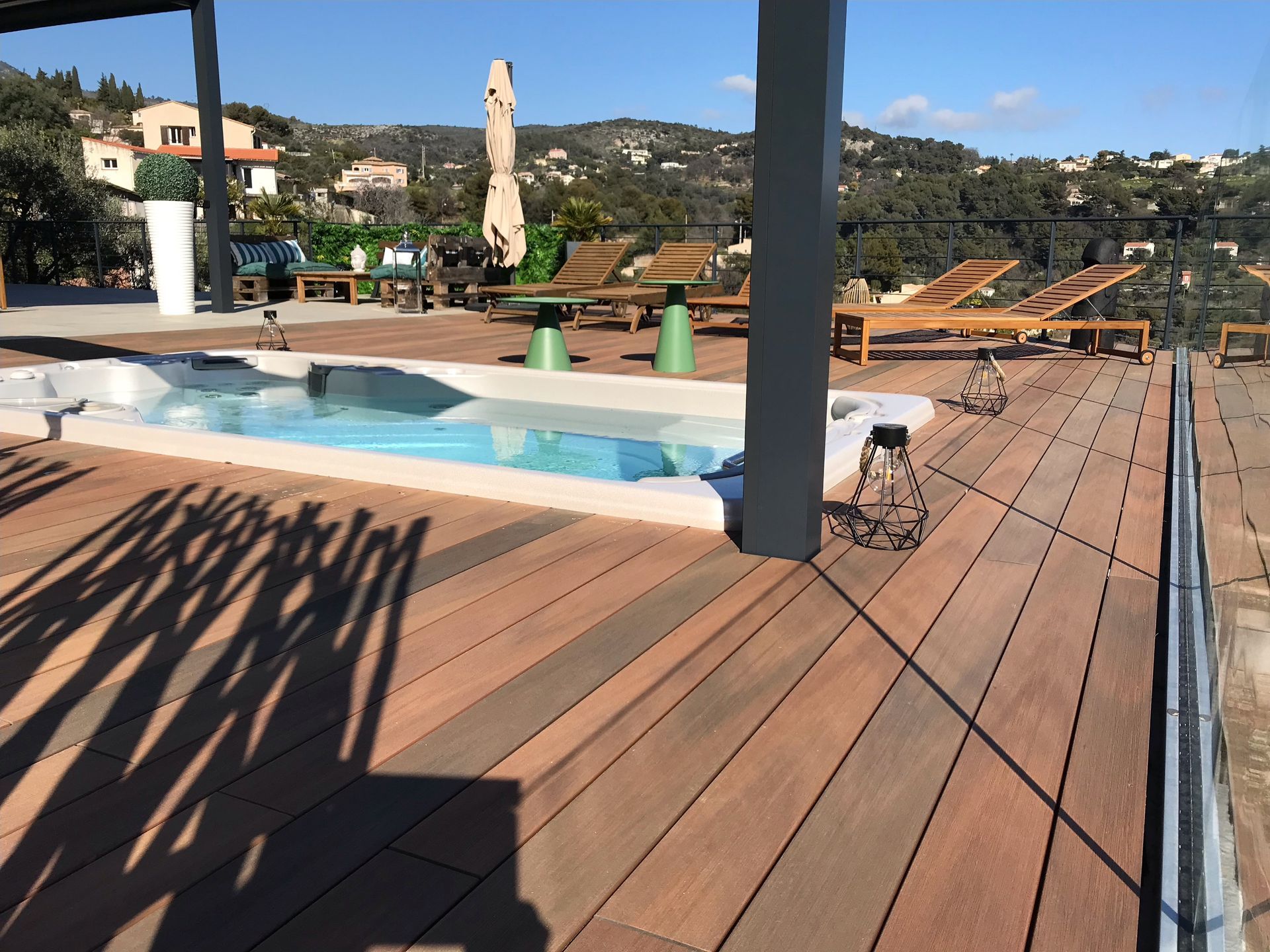 Une terrasse en bois avec une piscine en arrière-plan