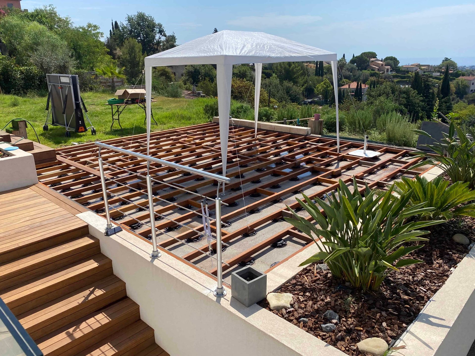 Une terrasse en bois avec des escaliers et une tente blanche au-dessus.