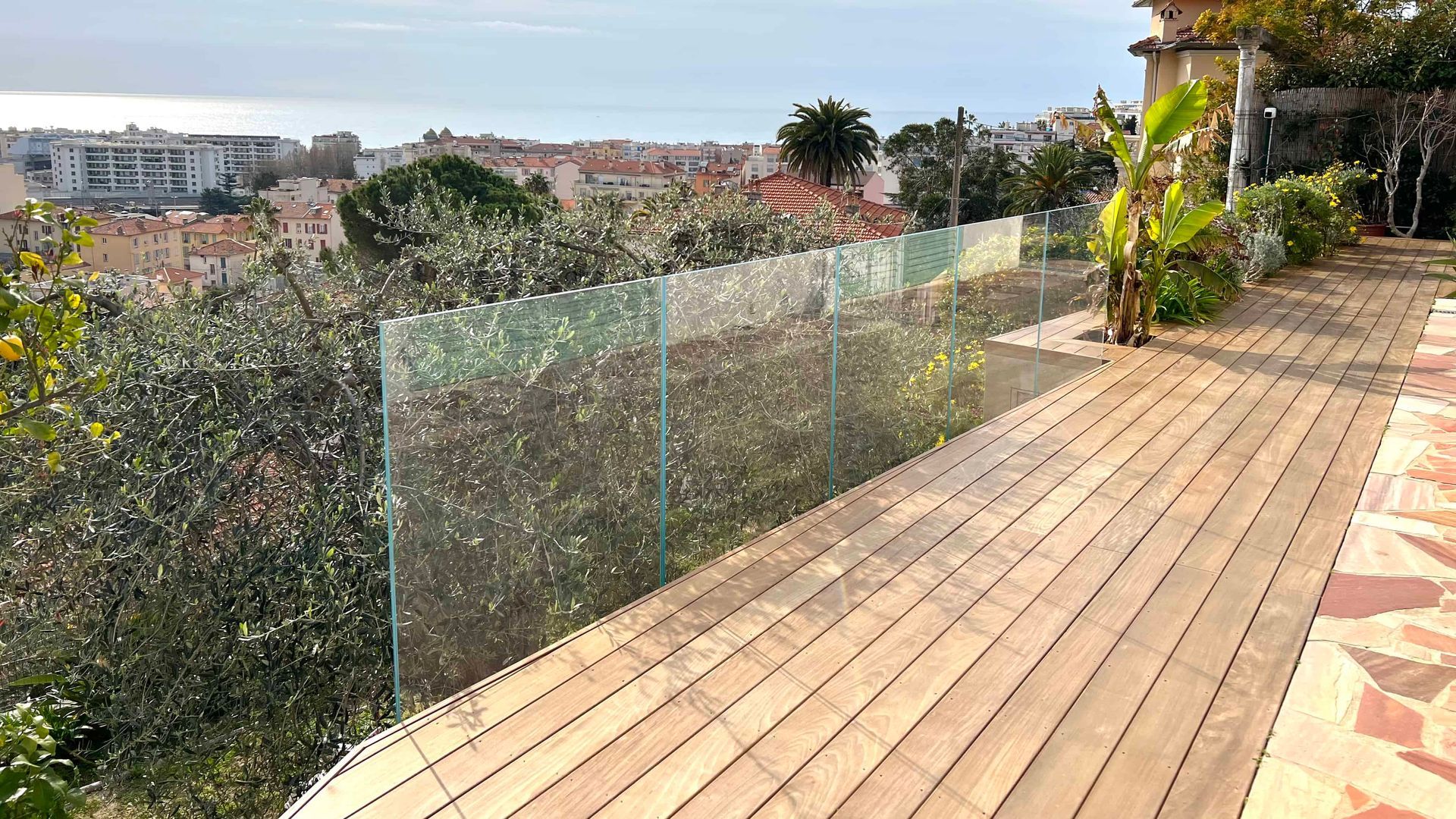 Une terrasse en bois avec une balustrade en verre et une vue sur l'océan.