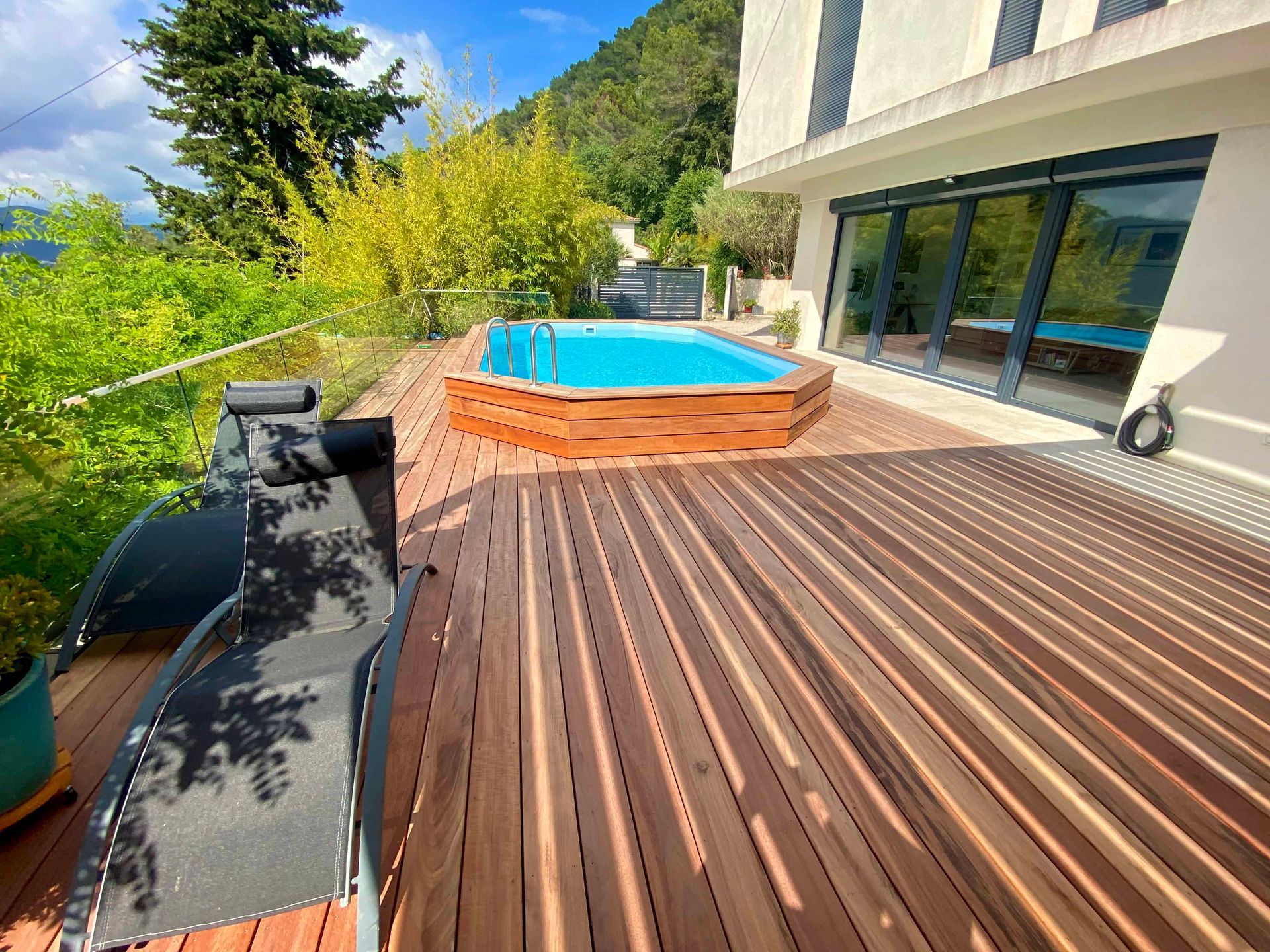 Une terrasse en bois avec une piscine en arrière-plan