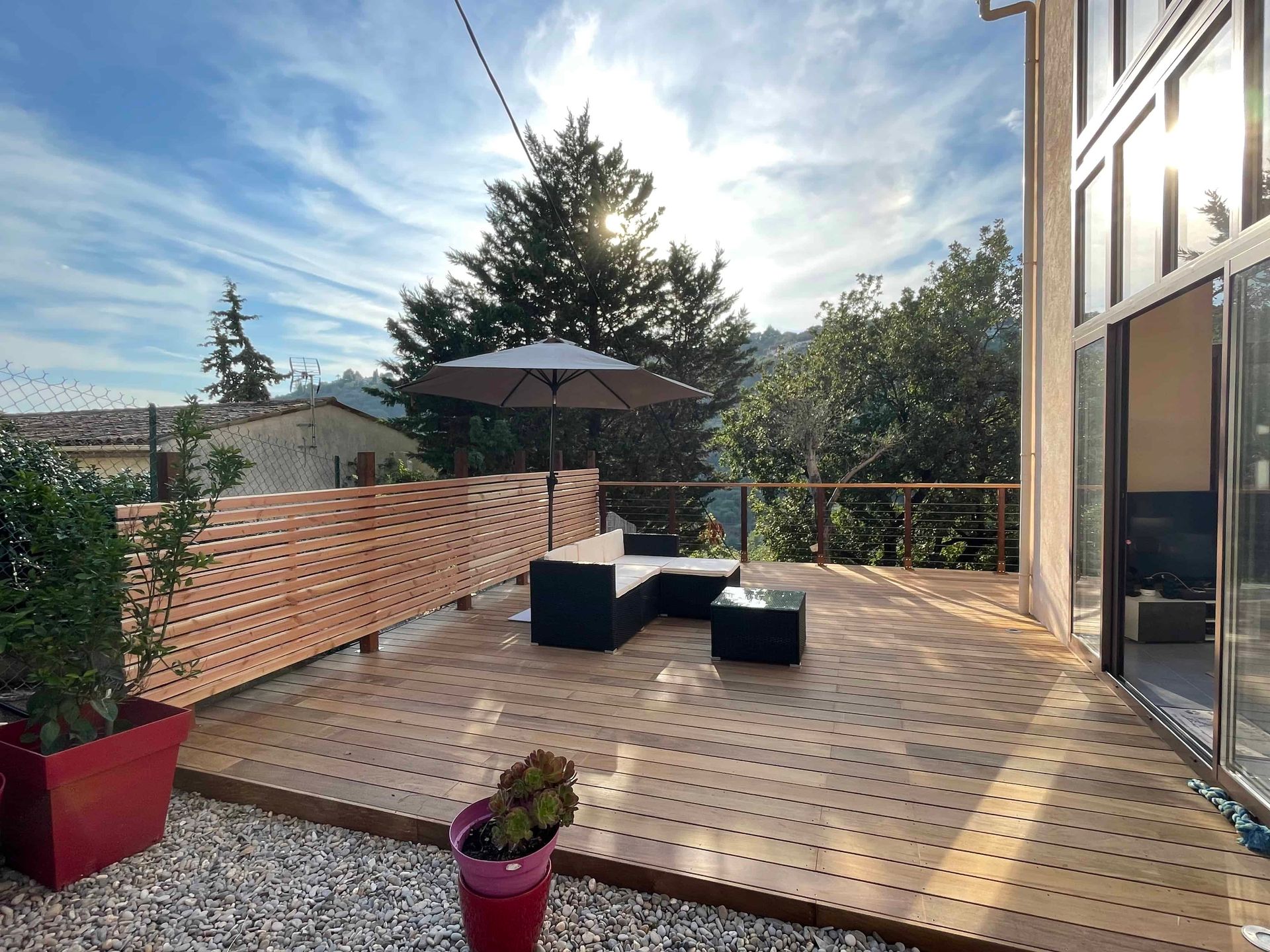 Une terrasse en bois IPE avec un canapé et un parasol dessus.