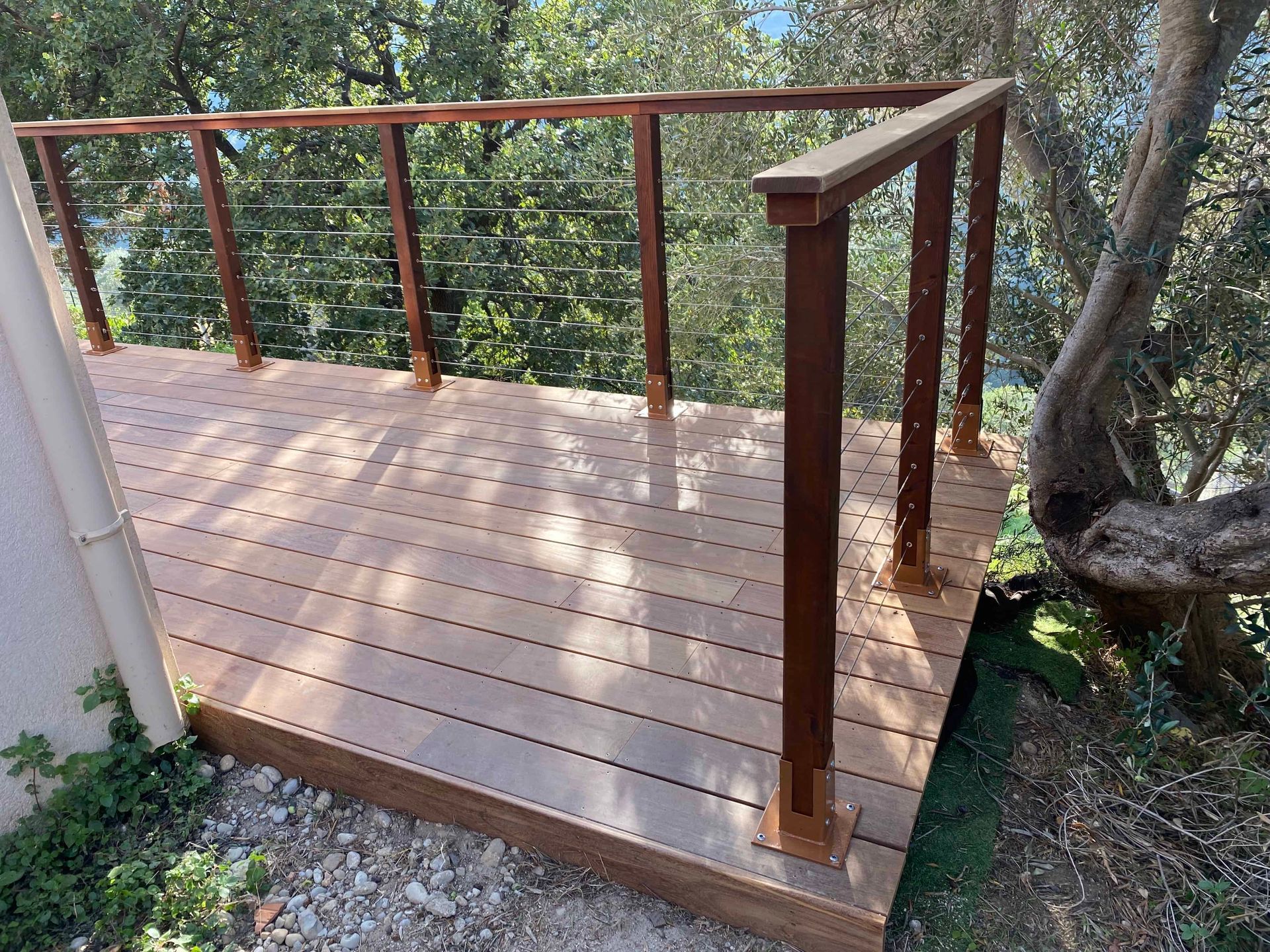 Une terrasse en bois IPE avec une balustrade en métal et des arbres en arrière-plan.