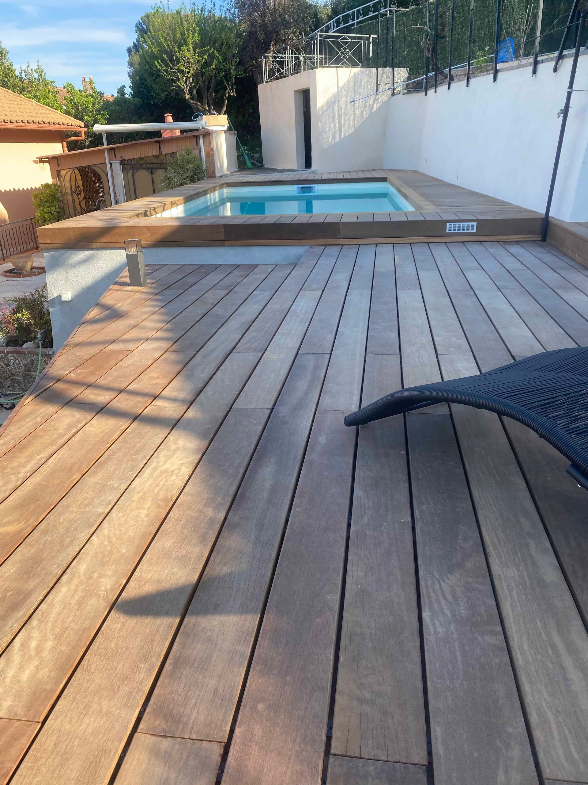 Une terrasse en bois avec une piscine en arrière-plan