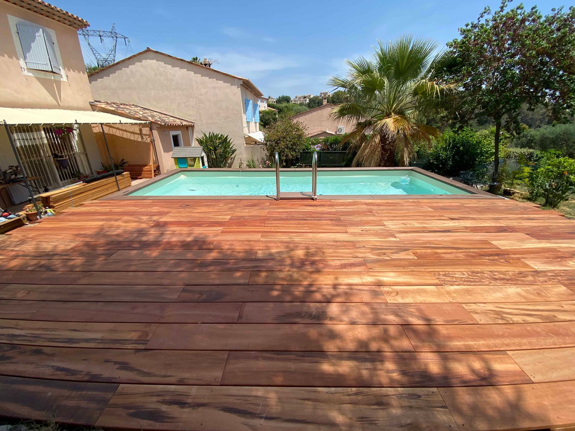 Une terrasse en bois avec une piscine en arrière-plan.