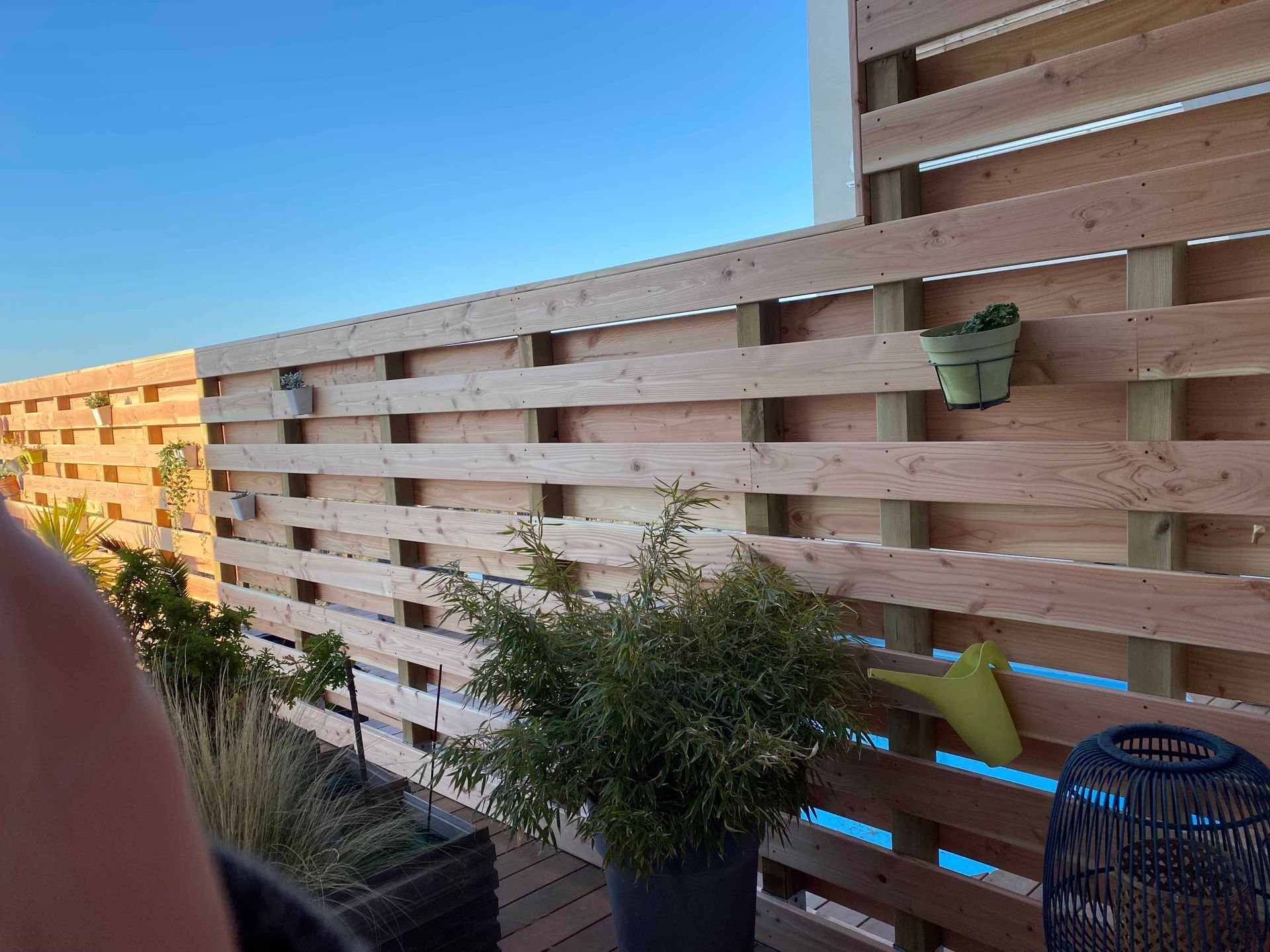 Une personne se tient sur un balcon avec une clôture en bois et des plantes en pot.