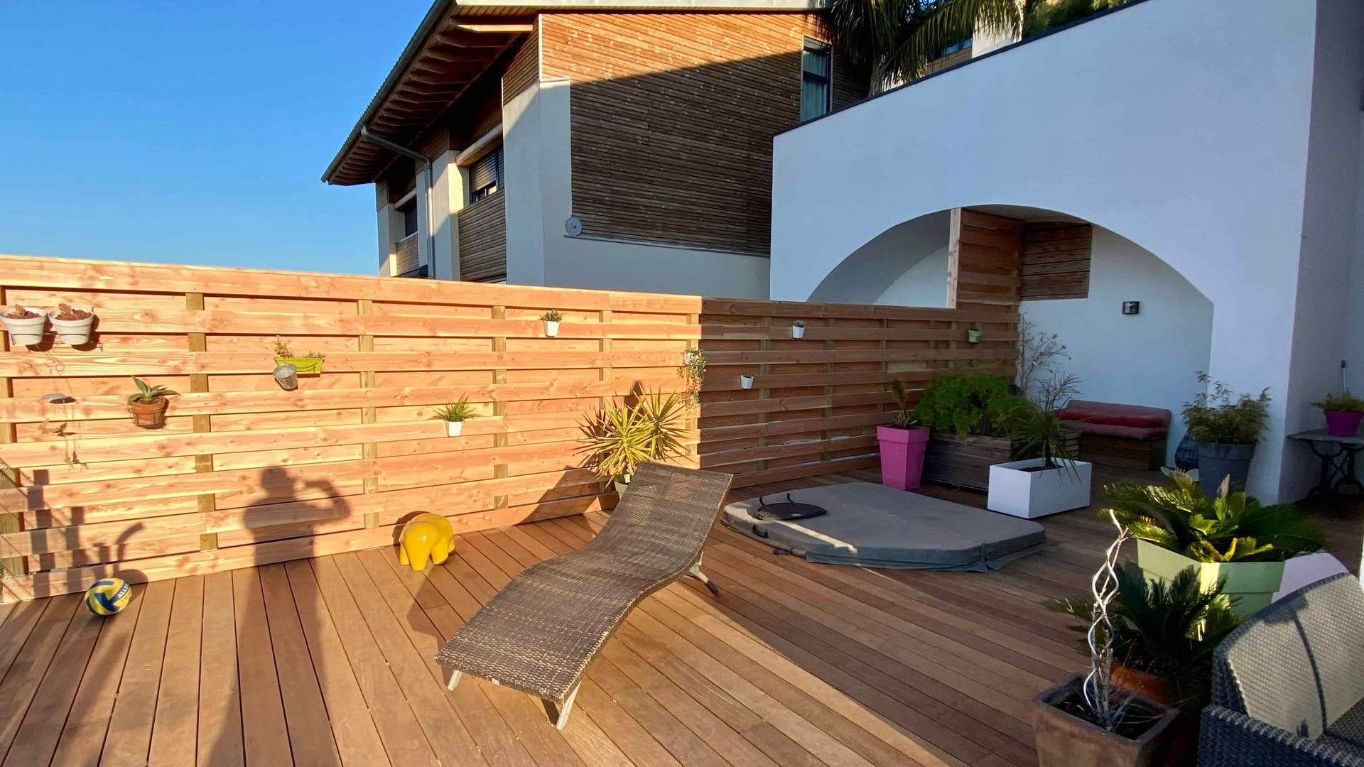 Une terrasse en bois avec des chaises et des plantes devant une maison