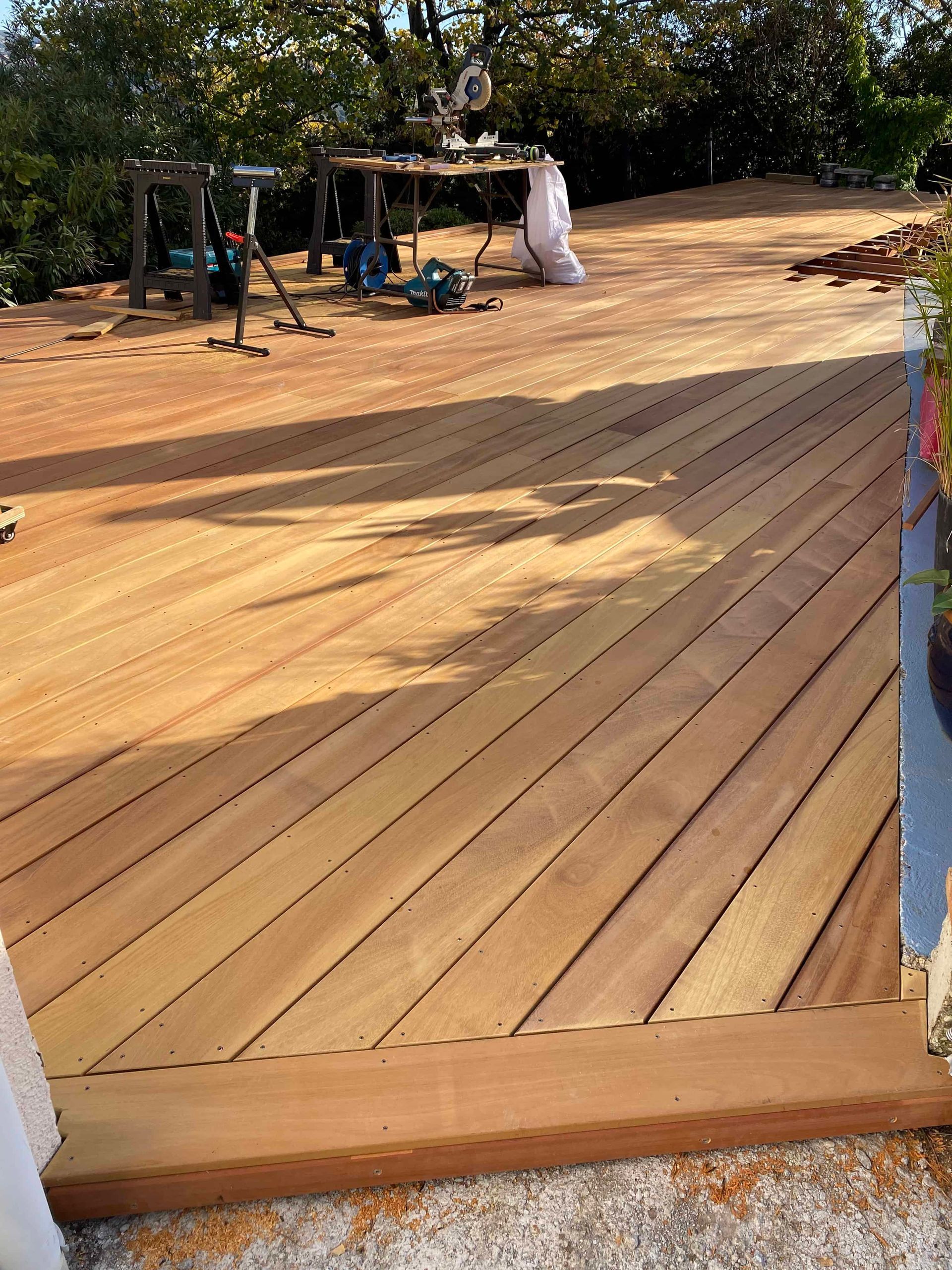 Une terrasse en bois est en cours de construction dans une cour avec des arbres en arrière-plan.
