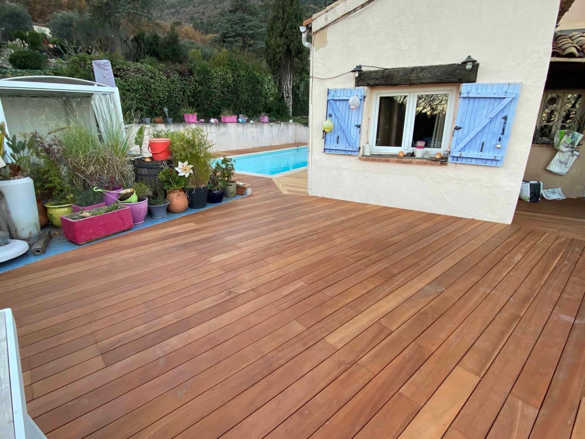 Une terrasse en bois devant une maison avec une piscine en arrière-plan.