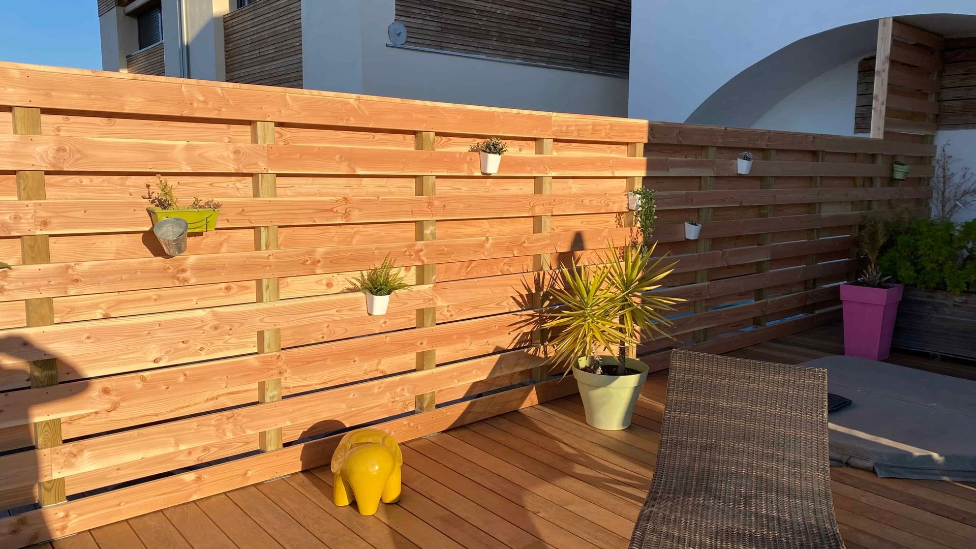 Une clôture en bois entoure une terrasse avec des chaises et des plantes en pot.