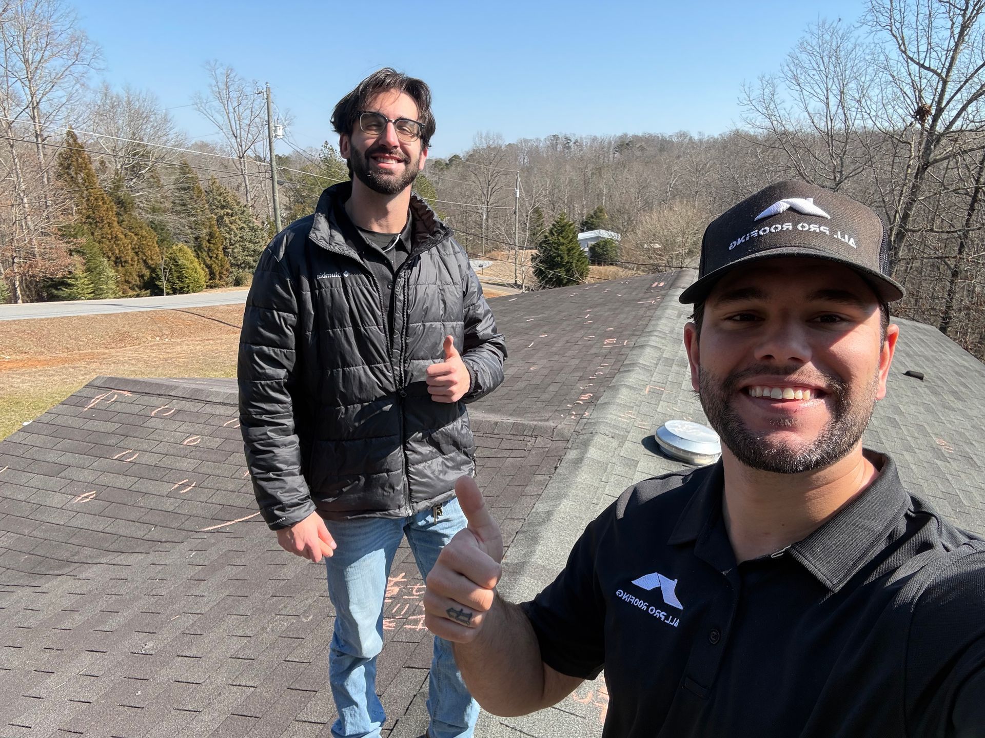 Two men smiling outdoors on a paved path, one giving a thumbs-up in the foreground.