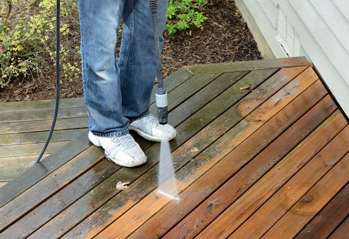 A person is cleaning a wooden deck with a high pressure washer.
