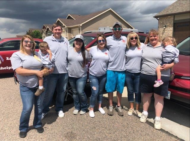 Group of people in matching shirts standing by red cars, posing outdoors on a sunny day.