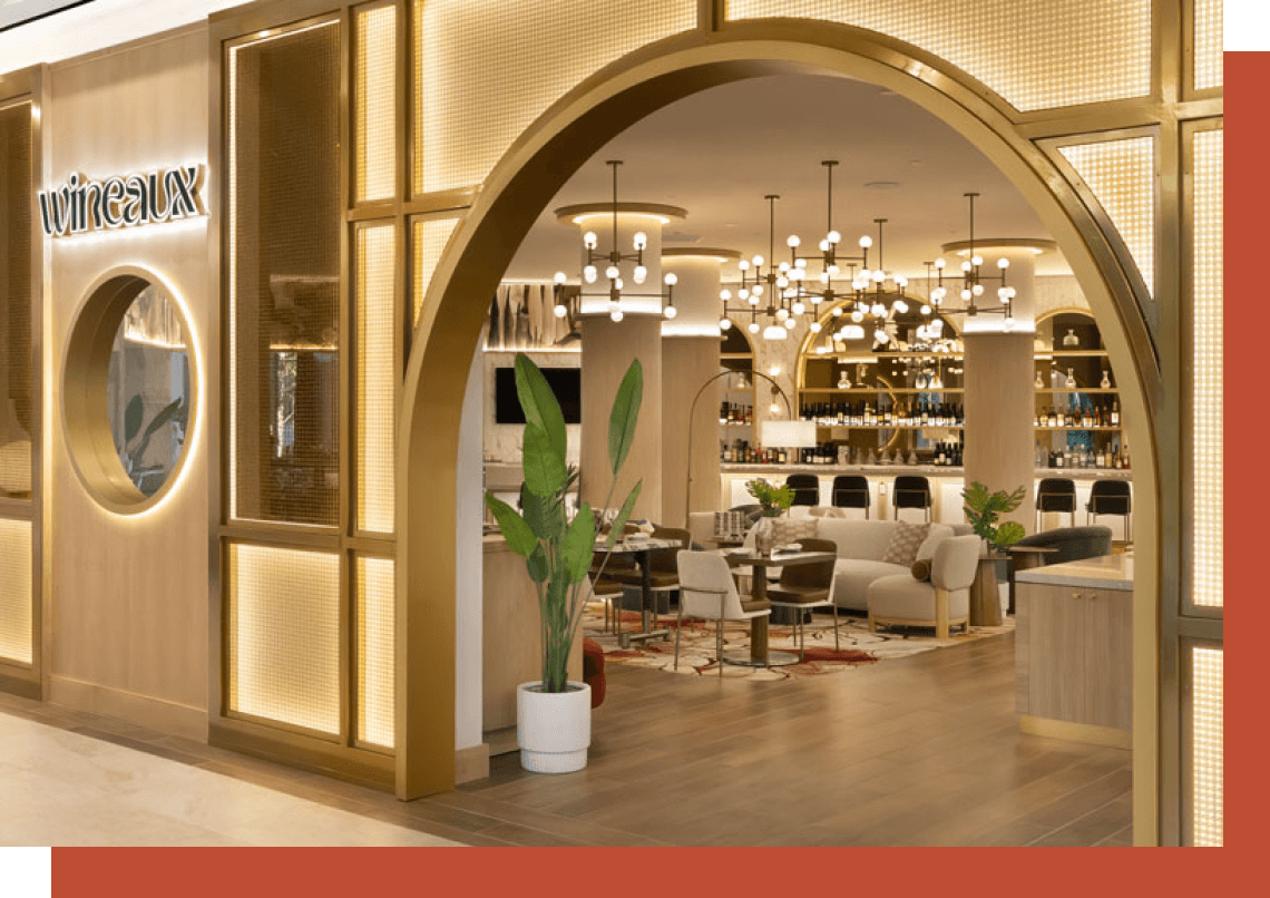 An arched entryway with brass trim leads to an upscale, brightly lit lounge featuring plush seating and elegant lighting.
