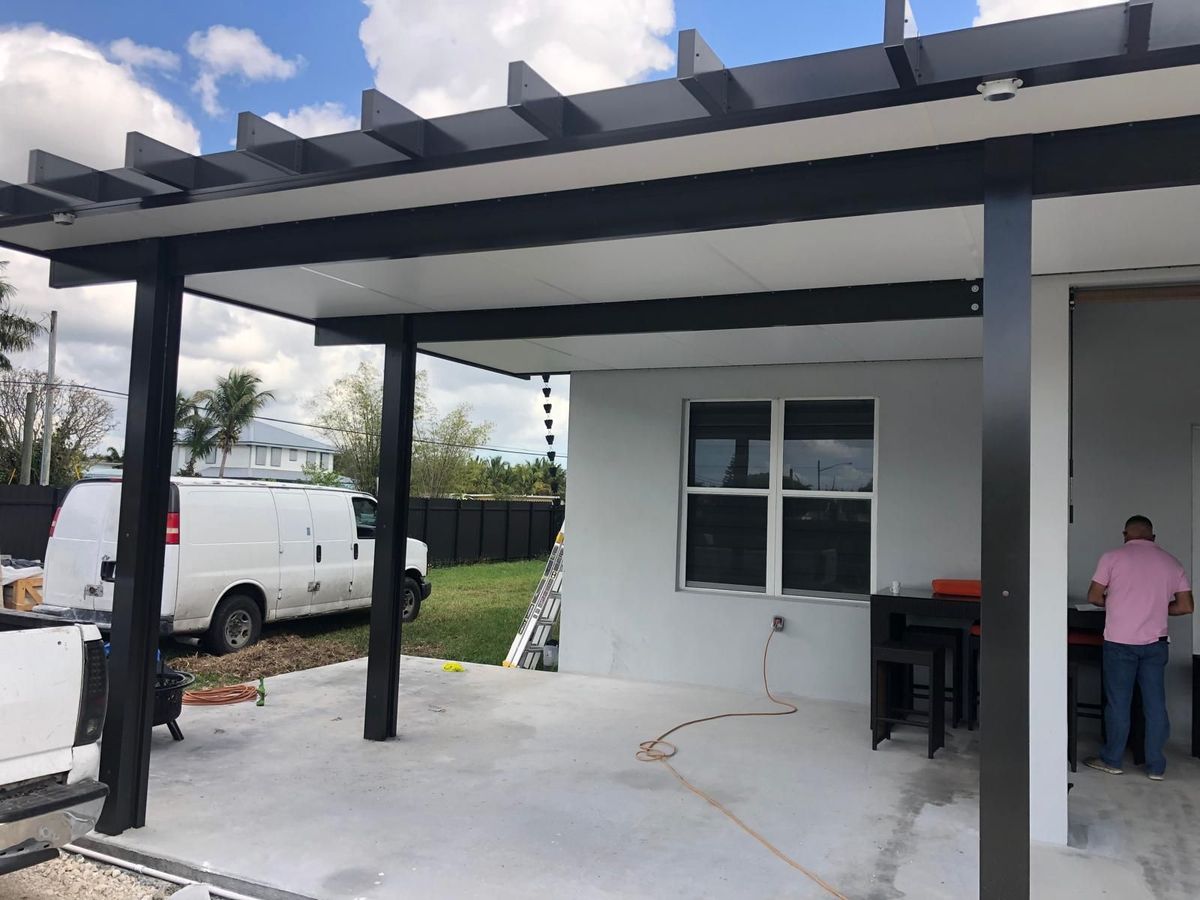 A man is standing under a pergola on the side of a house.