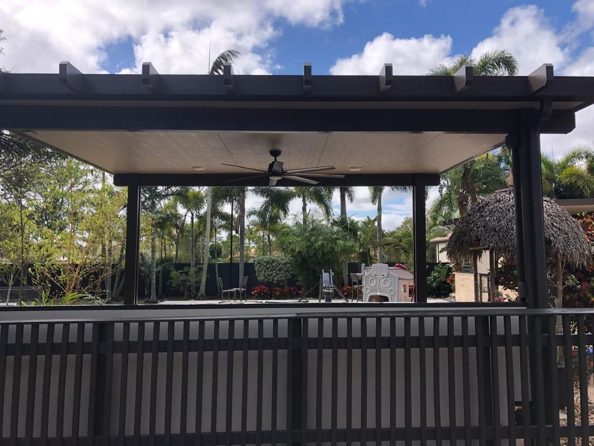 A pergola with a ceiling fan and a fence in the background.