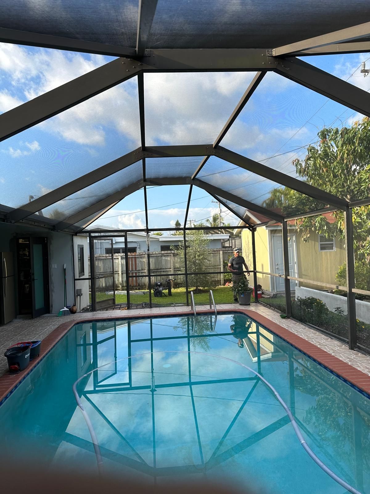 A man is standing next to a swimming pool in a screened in area.