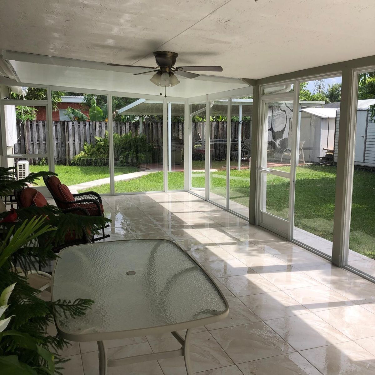 A screened in porch with a table and chairs and a ceiling fan