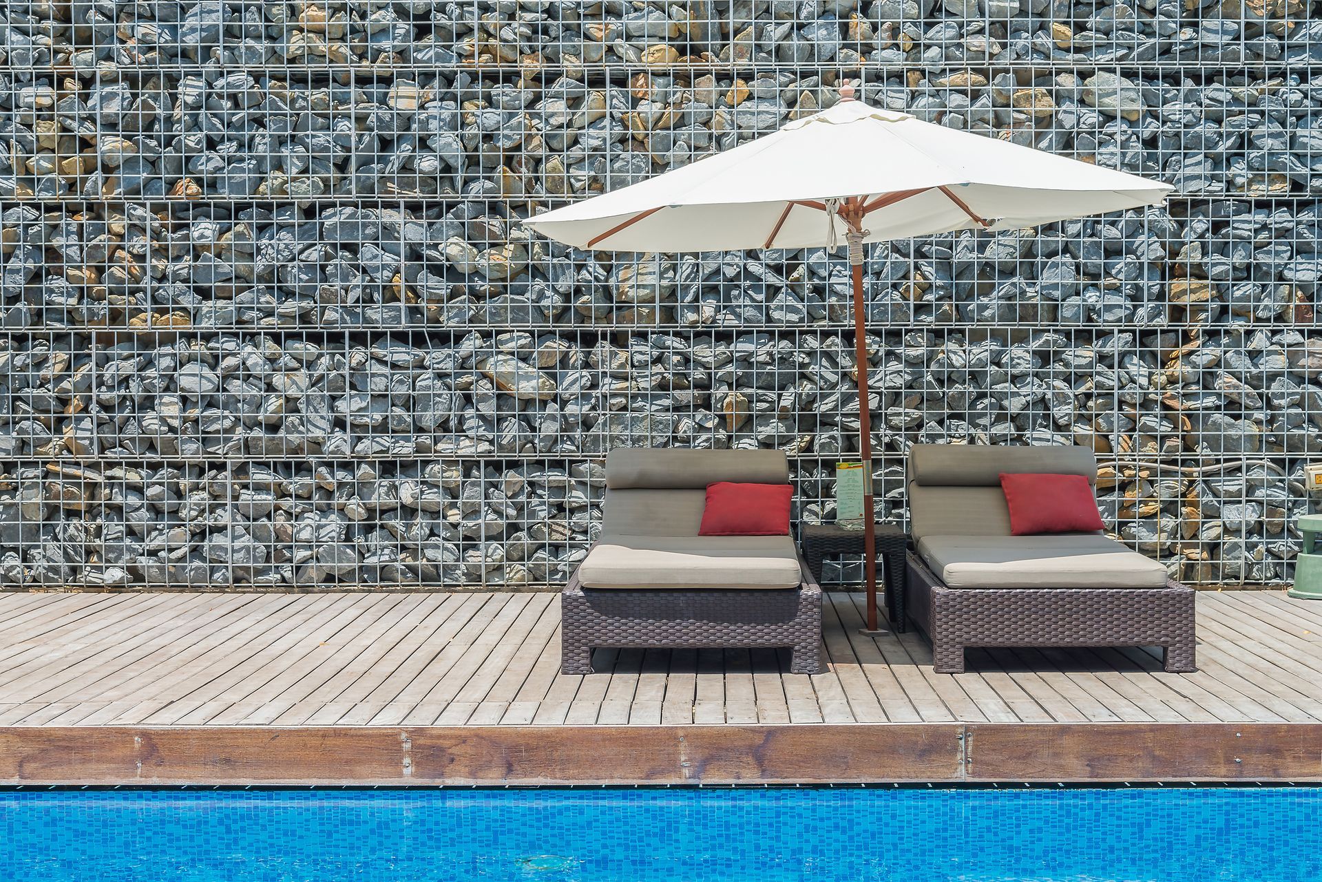 Two lounge chairs under an umbrella next to a swimming pool