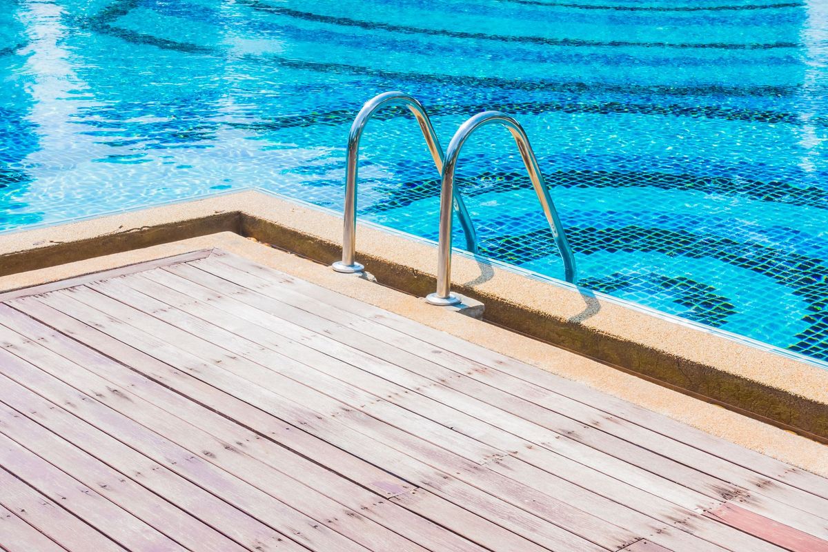 A swimming pool with a wooden deck and stairs leading to it.