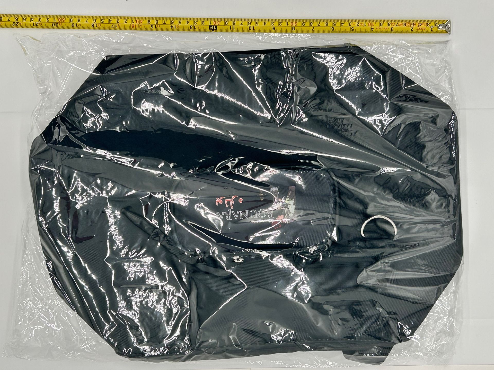 Black zippered bag in clear plastic packaging with a yellow measuring tape above it.