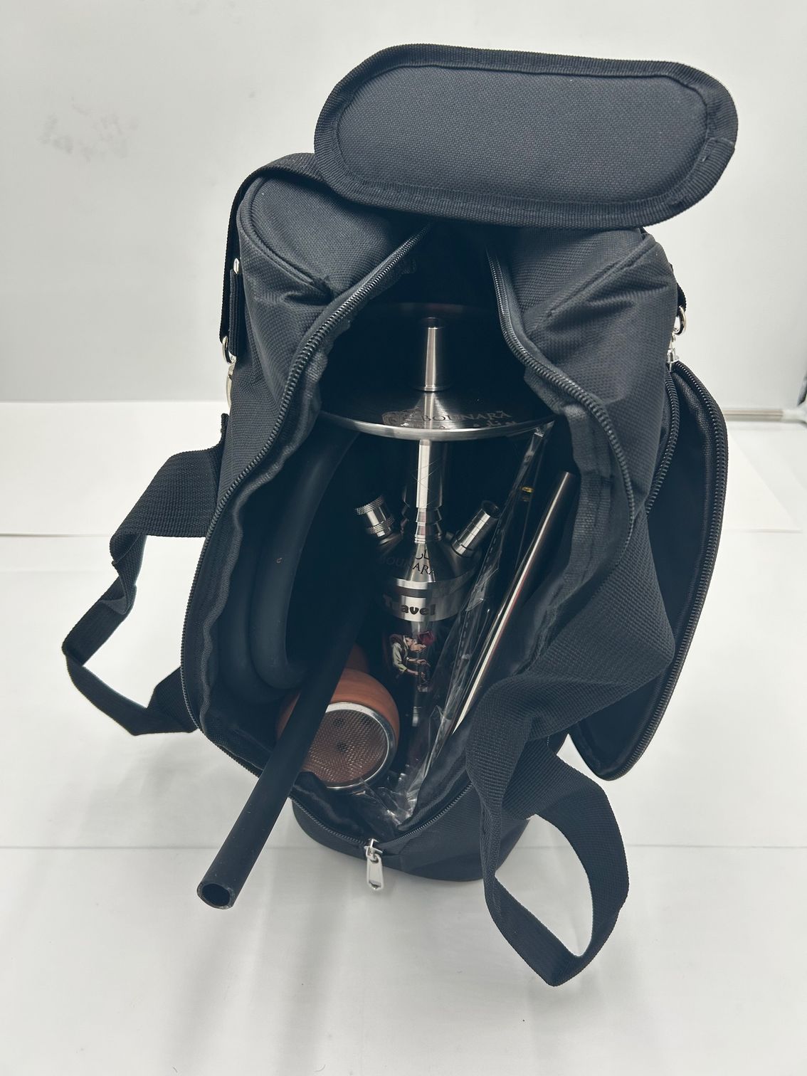 Black backpack open with shiny metal hookah components inside on a white background