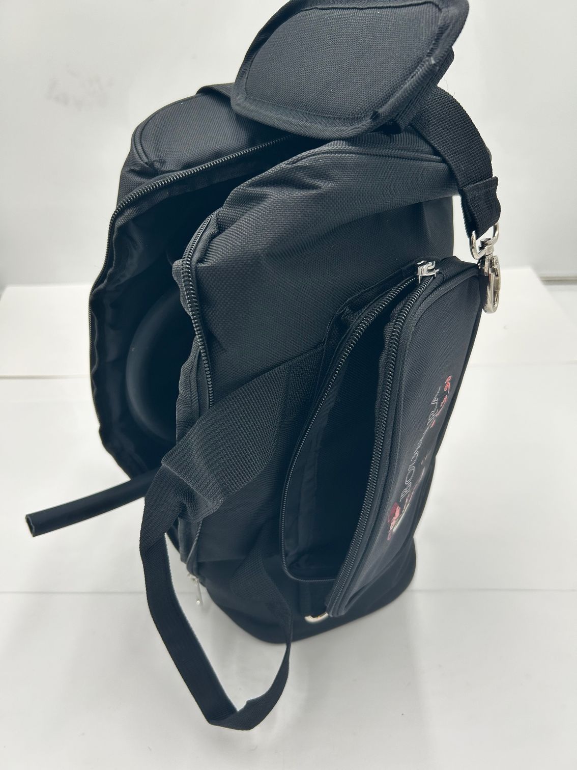 Black backpack standing open on a white surface, with padded shoulder straps and side pockets.