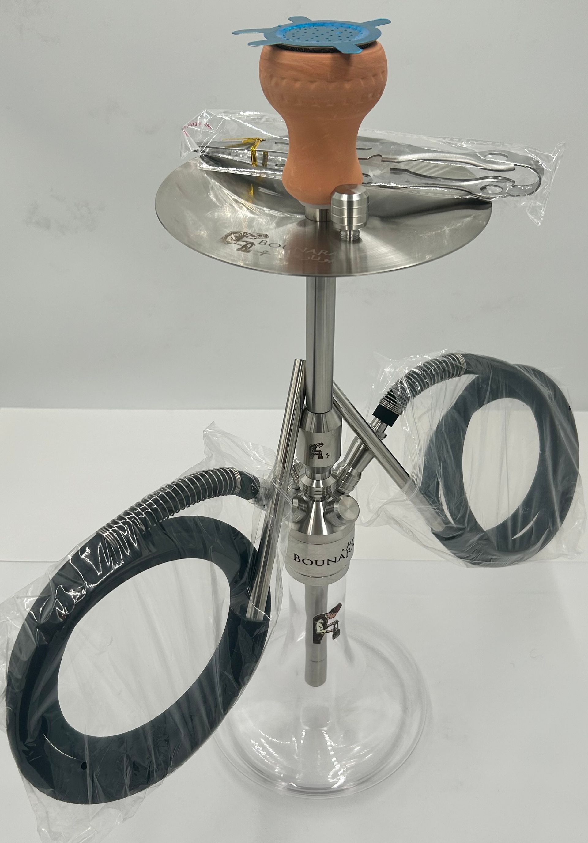 A silver hookah with a clay bowl, two hoses, and a clear glass base, set on a white surface.
