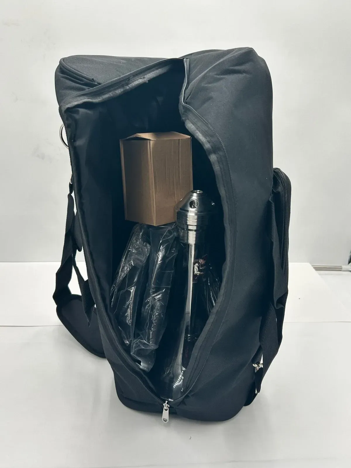 Black backpack open, revealing a box and items wrapped in black plastic.