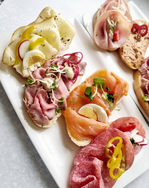 Verschiedene offene Sandwiches auf einer weißen Platte; Fleisch, Käse, Eier und Gemüse auf geröstetem Brot.