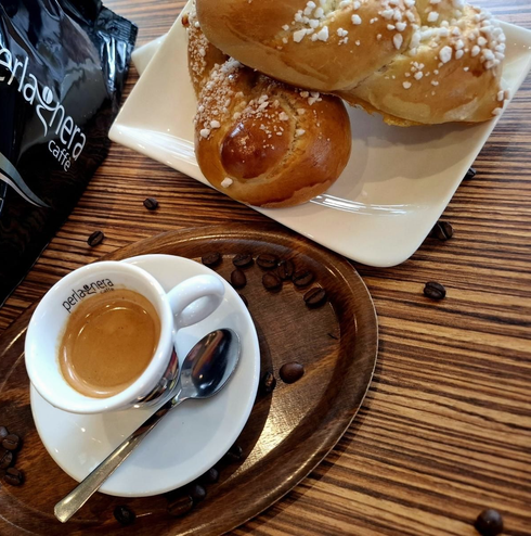 Espresso in der Tasse mit Gebäck und Kaffeebohnen auf einem Holztablett und Tisch.