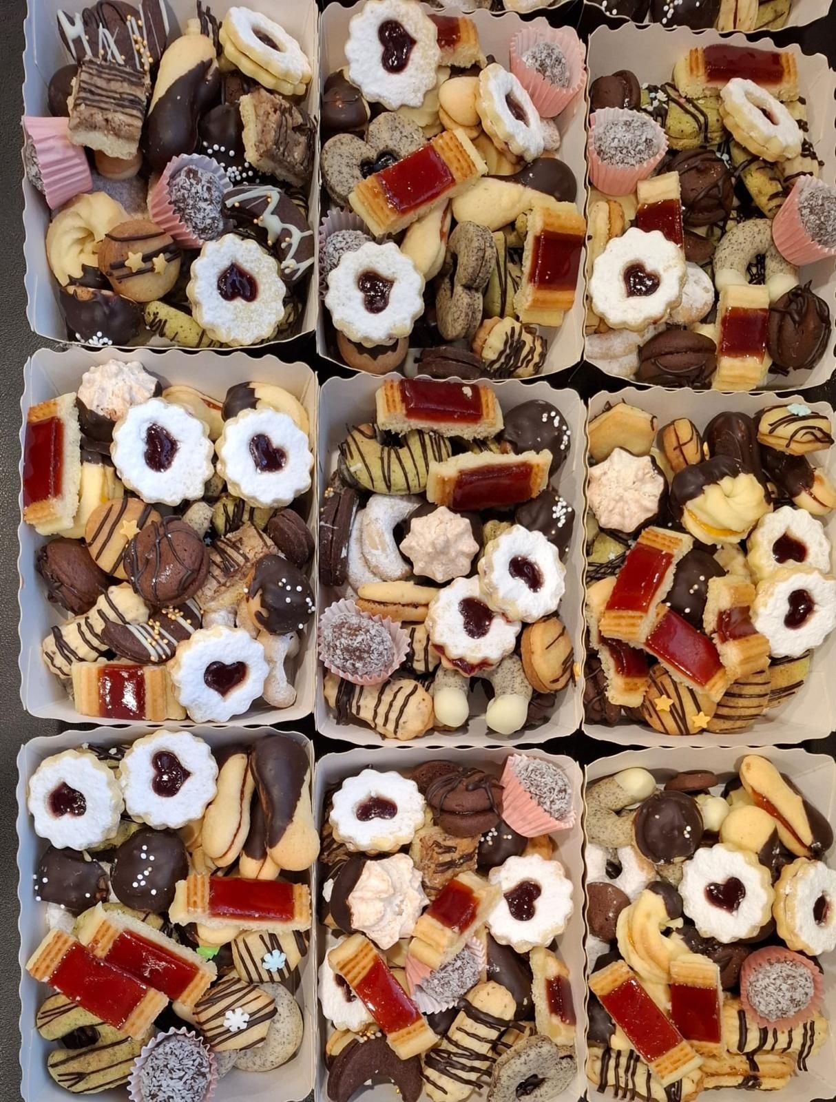 Neun Schachteln mit verschiedenen Kekssorten, darunter mit Marmelade gefüllte, schokoladenüberzogene und mit Streuseln bestreute Kekse.