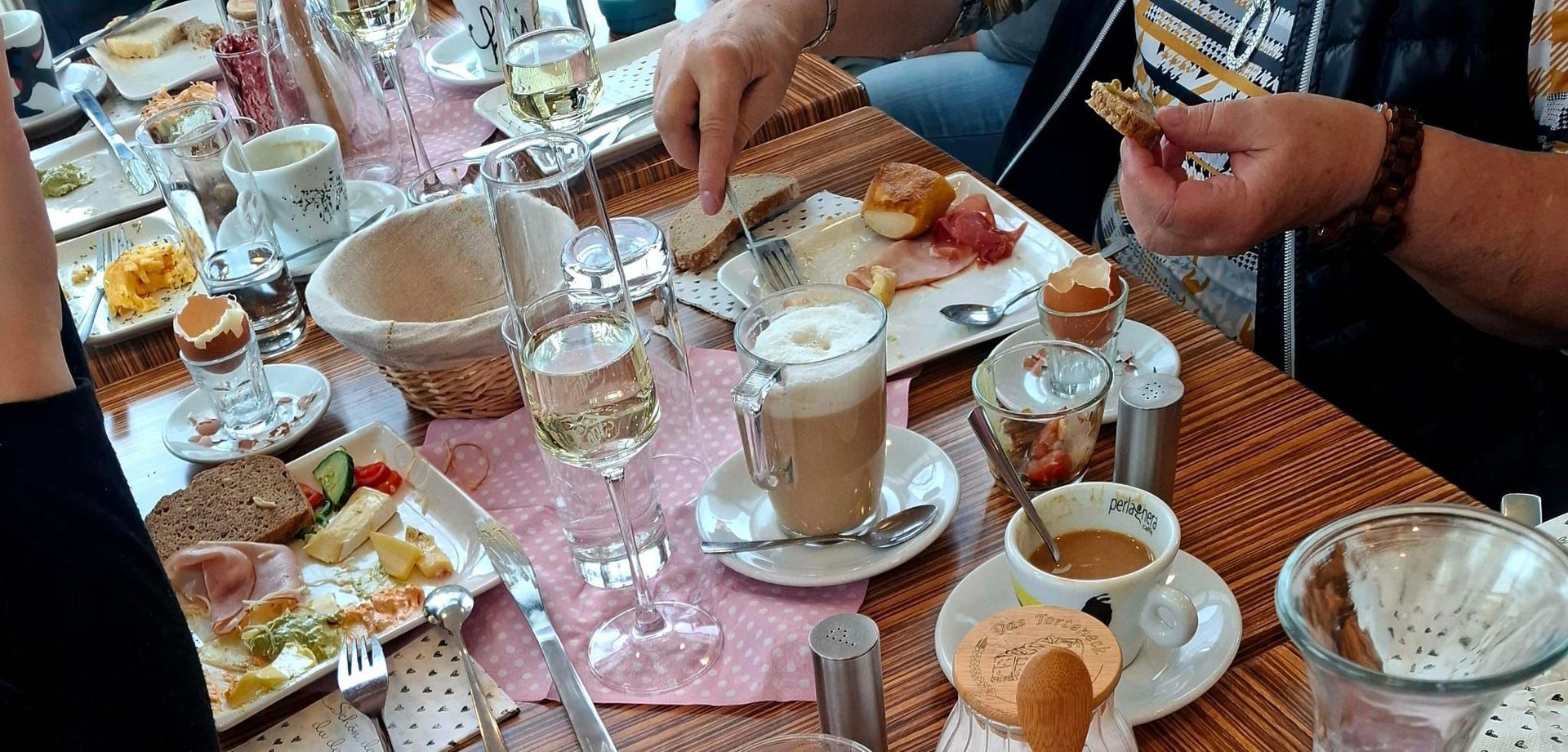 Ein für eine Mahlzeit gedeckter Tisch mit mehreren Tellern Essen, Getränken und essenden Personen.