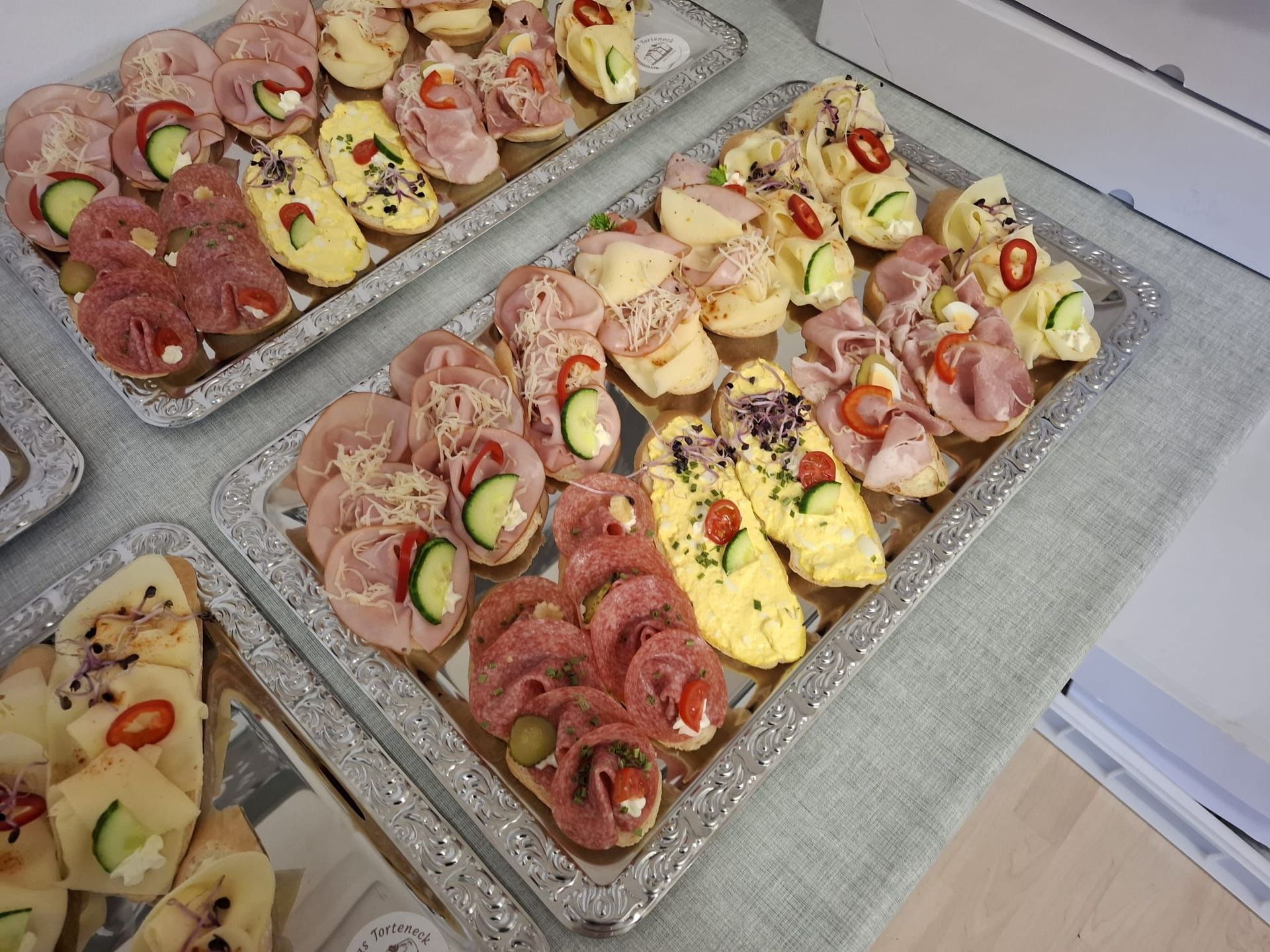 Platten mit verschiedenen Canapés: Salamiröllchen, Schinken-Gurken-Häppchen sowie Eier- und Tomatenbelag.